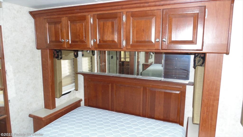 RV rental bedroom: cozy bed with overhead wood cabinets, mirrored headboard, and convenient side storage.. THOR Four Winds Infinity 2005