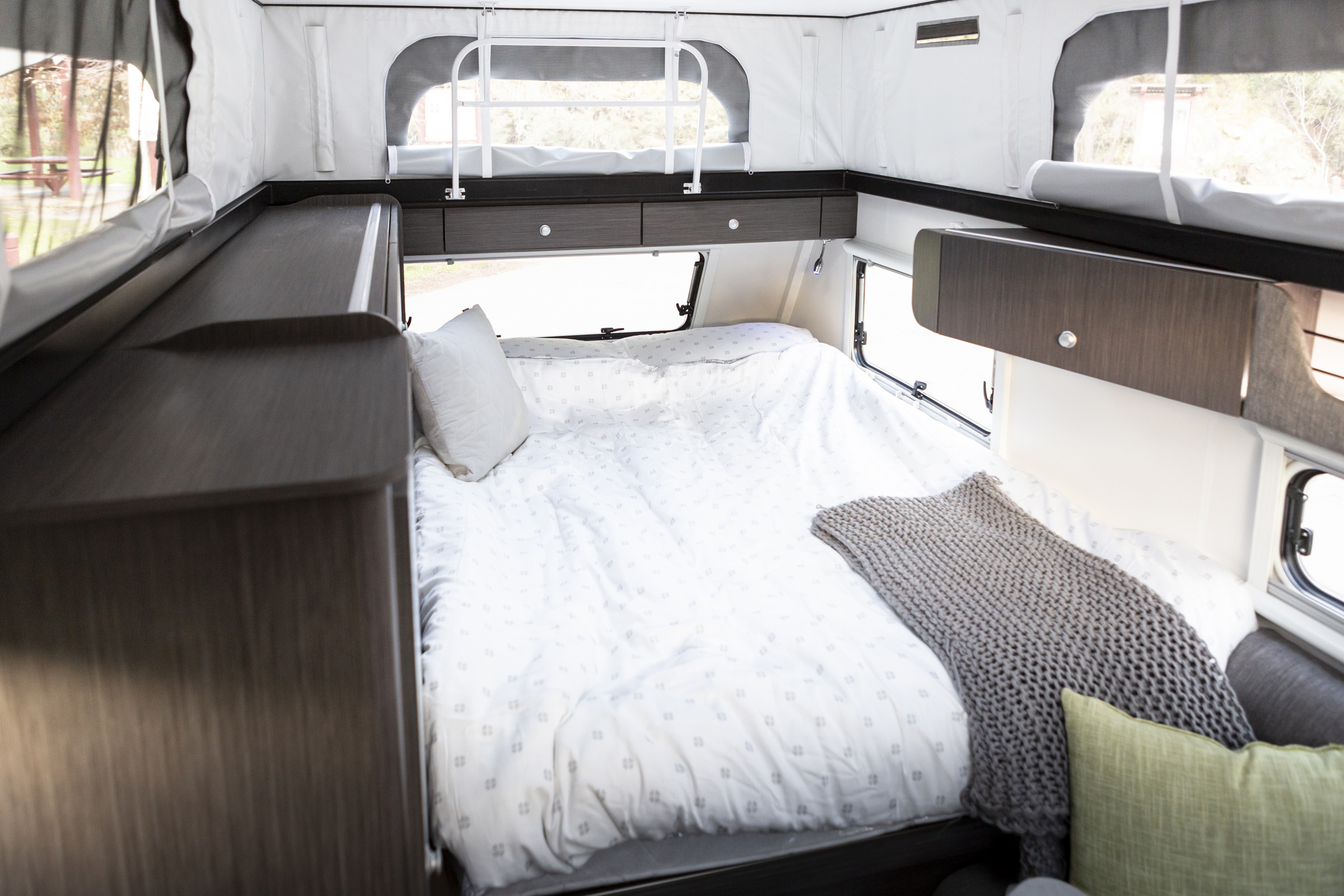 Inside this RV rental: a large, comfortable bed with white bedding, built-in storage, and bright windows.. Jayco CrossTrak 2022