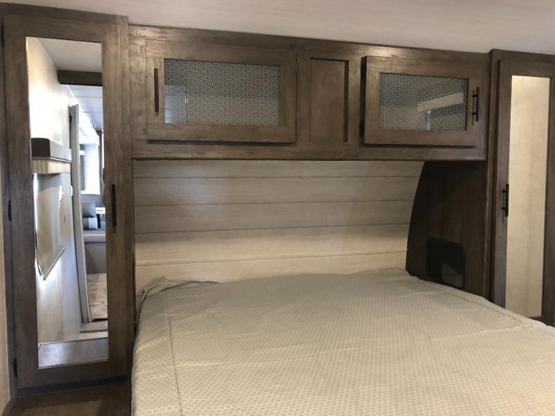 RV rental bedroom: light wood headboard, overhead cabinets with patterned glass, and mirrored wardrobe doors.. Forest River Salem 2021