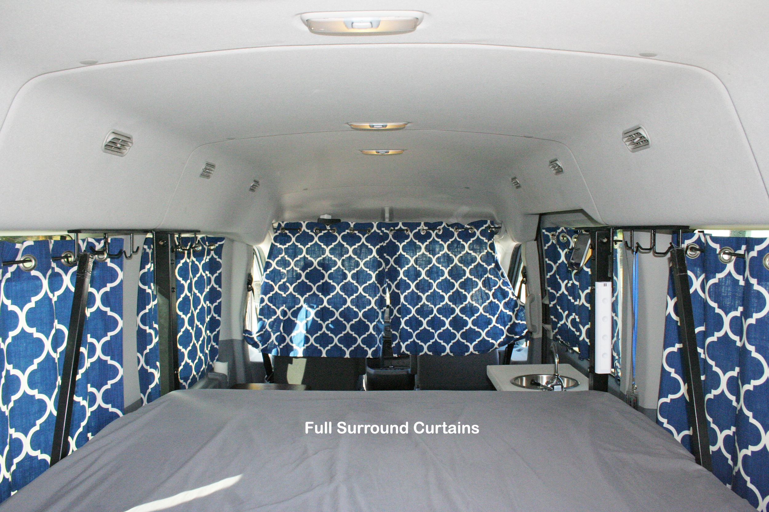 RV rental: Camper van interior featuring a comfortable bed, small sink, and full surround blue patterned privacy curtains.. Ford Transit 2021