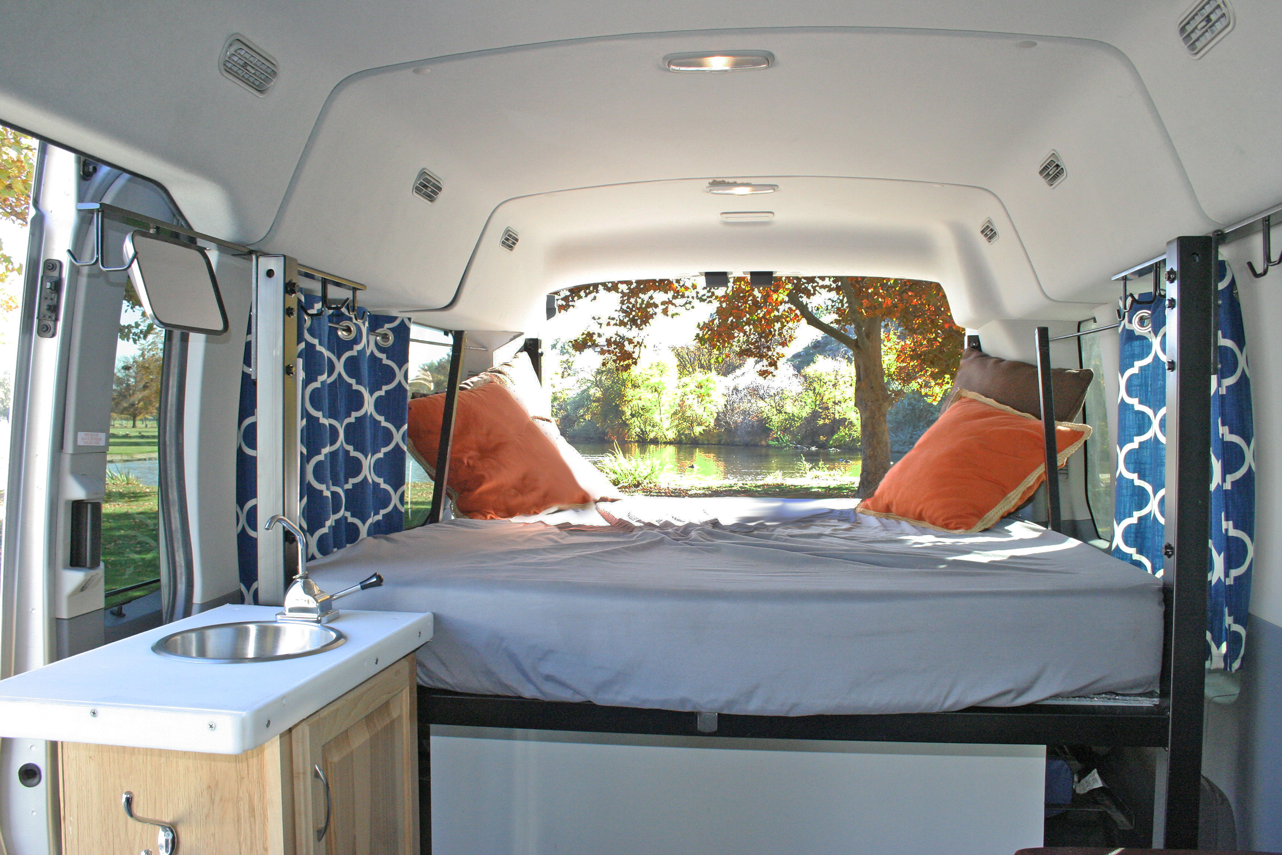 Cozy RV rental interior with a bed, small sink, and scenic view of a pond and trees from the rear.. Ford Transit 2021