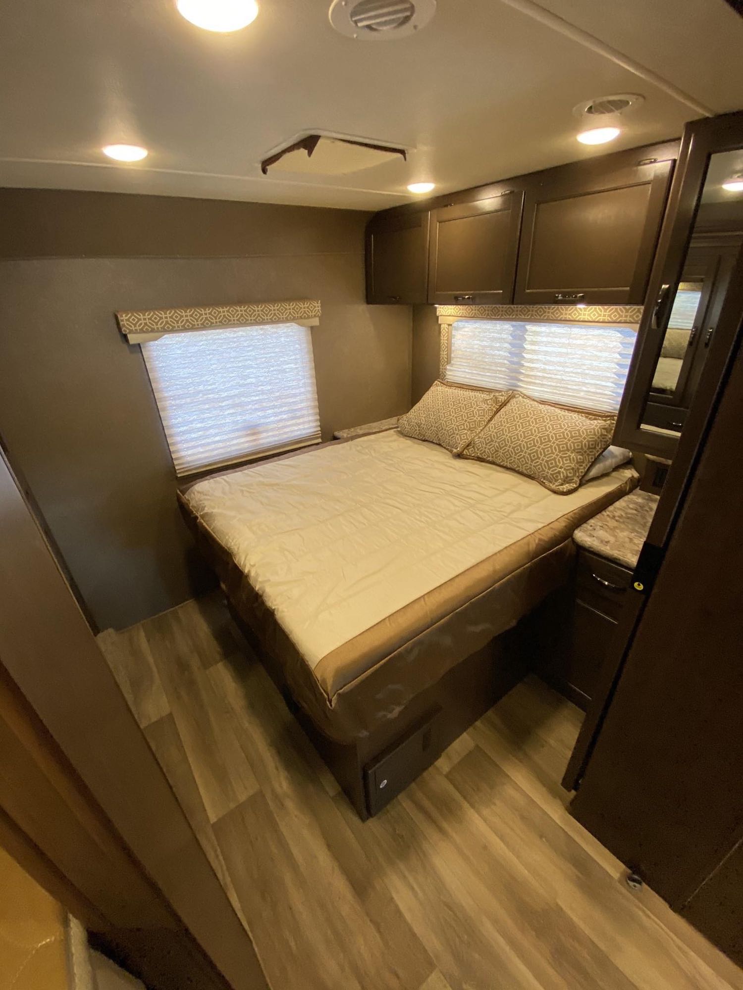 Experience comfort in this RV rental bedroom: a cozy bed, dual windows, overhead cabinets, and wood-look flooring.. Thor Motor Coach Freedom Elite 2019