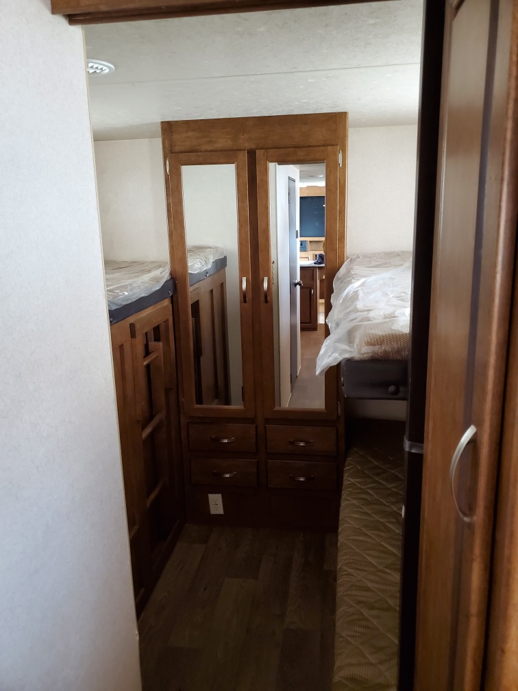 RV rental interior: A compact hallway features bunk beds (left), a mirrored wardrobe (center), and another bed (right).. Forest River Wildwood X-Lite 2018