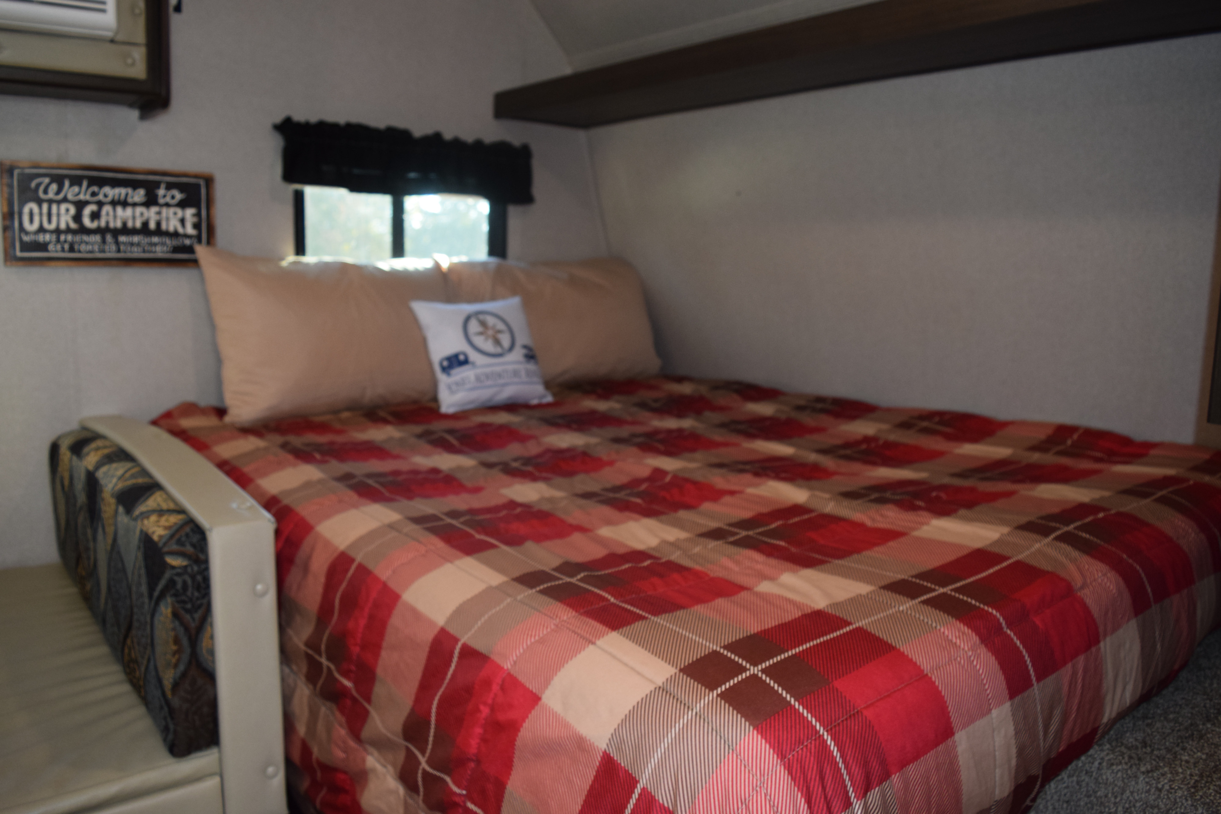 Cozy RV rental bedroom featuring a comfy bed with plaid bedding, pillows, and a 'Welcome to Our Campfire' sign.. Keystone Springdale 2019