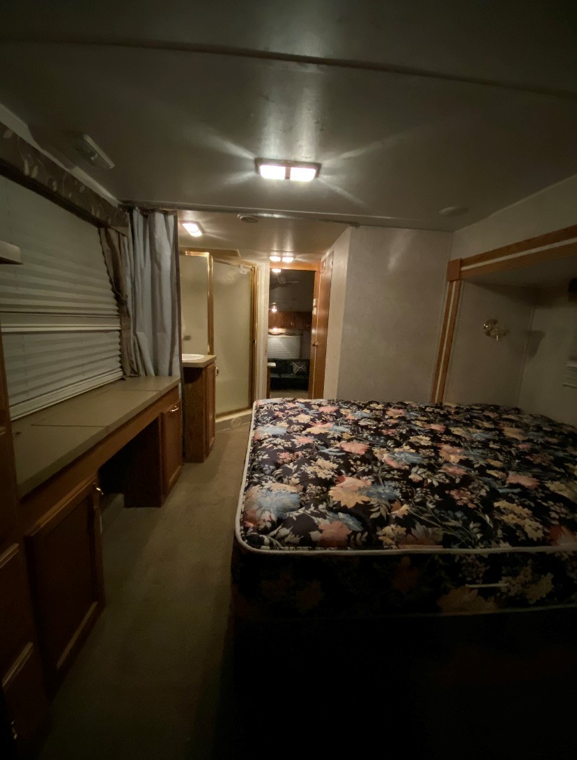 An RV rental's compact interior: a dark floral bed, a built-in desk area, and a glimpse of the bathroom beyond.. Forest River Other 2012