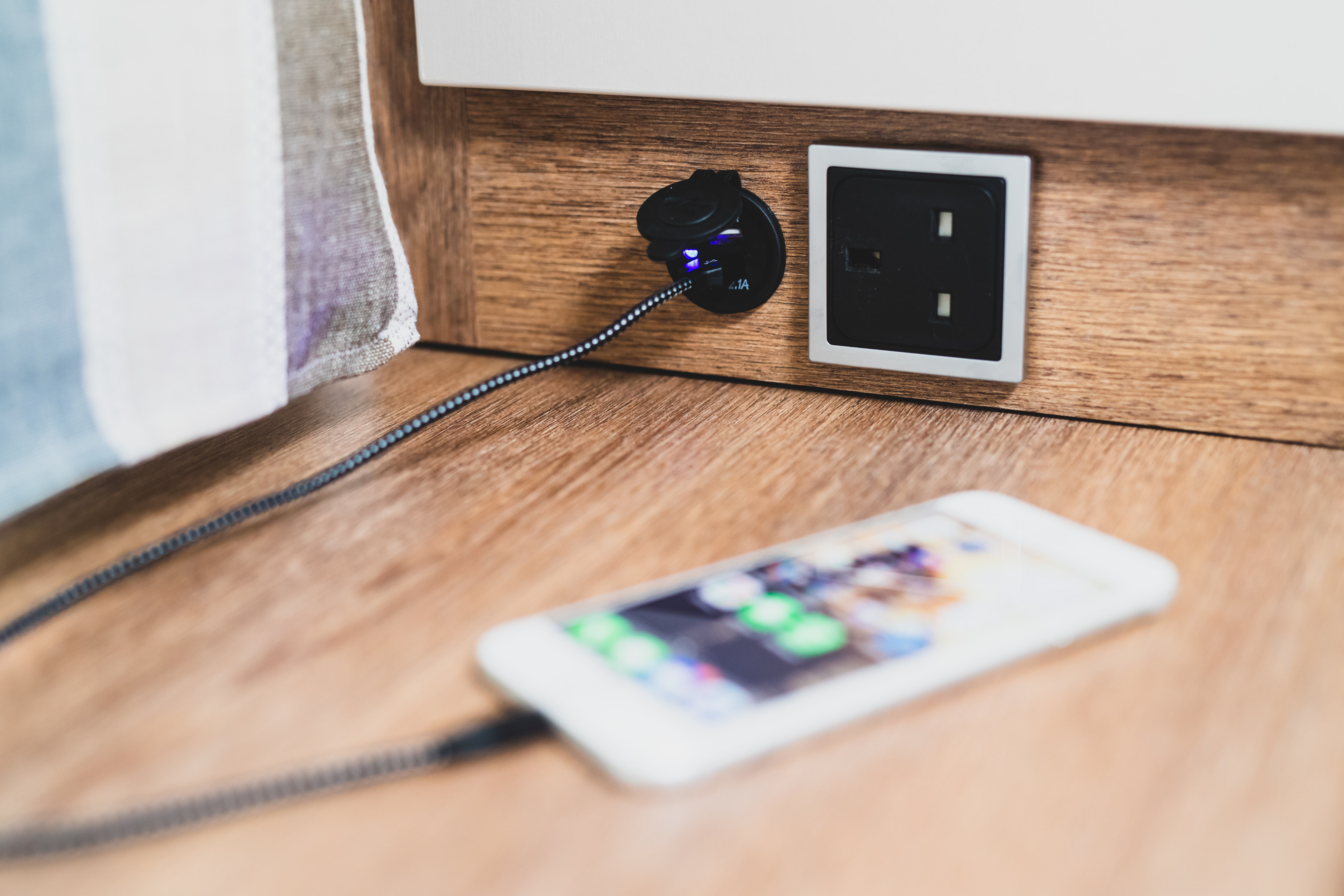 A smartphone charges via an integrated USB port, next to a power outlet, found in a modern rv rental interior.. GlamperRV DBL 2025