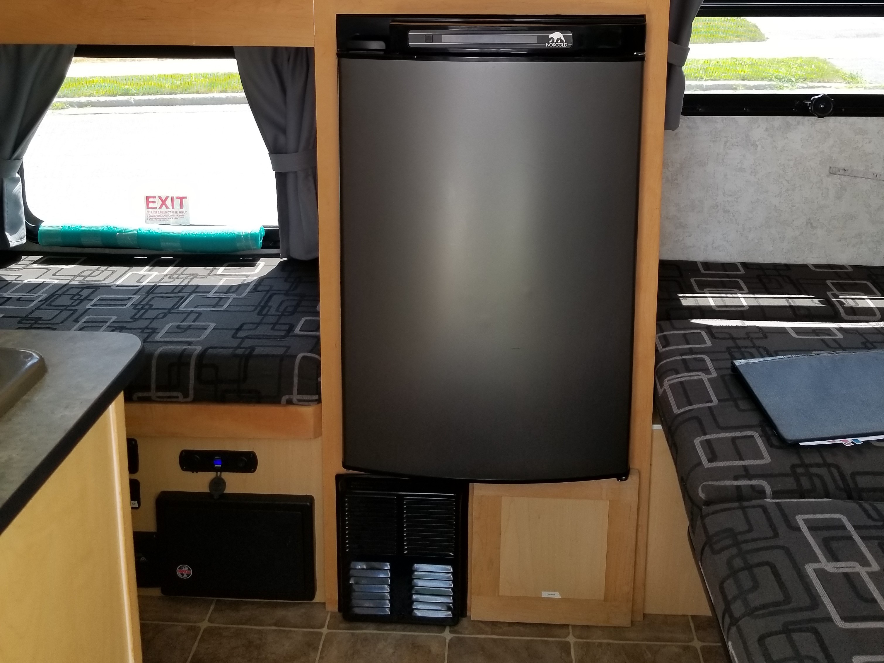 RV rental interior: Norcold refrigerator, patterned seating, and an emergency exit window with blue foam padding.. Prolite Prolite Trailer 2015