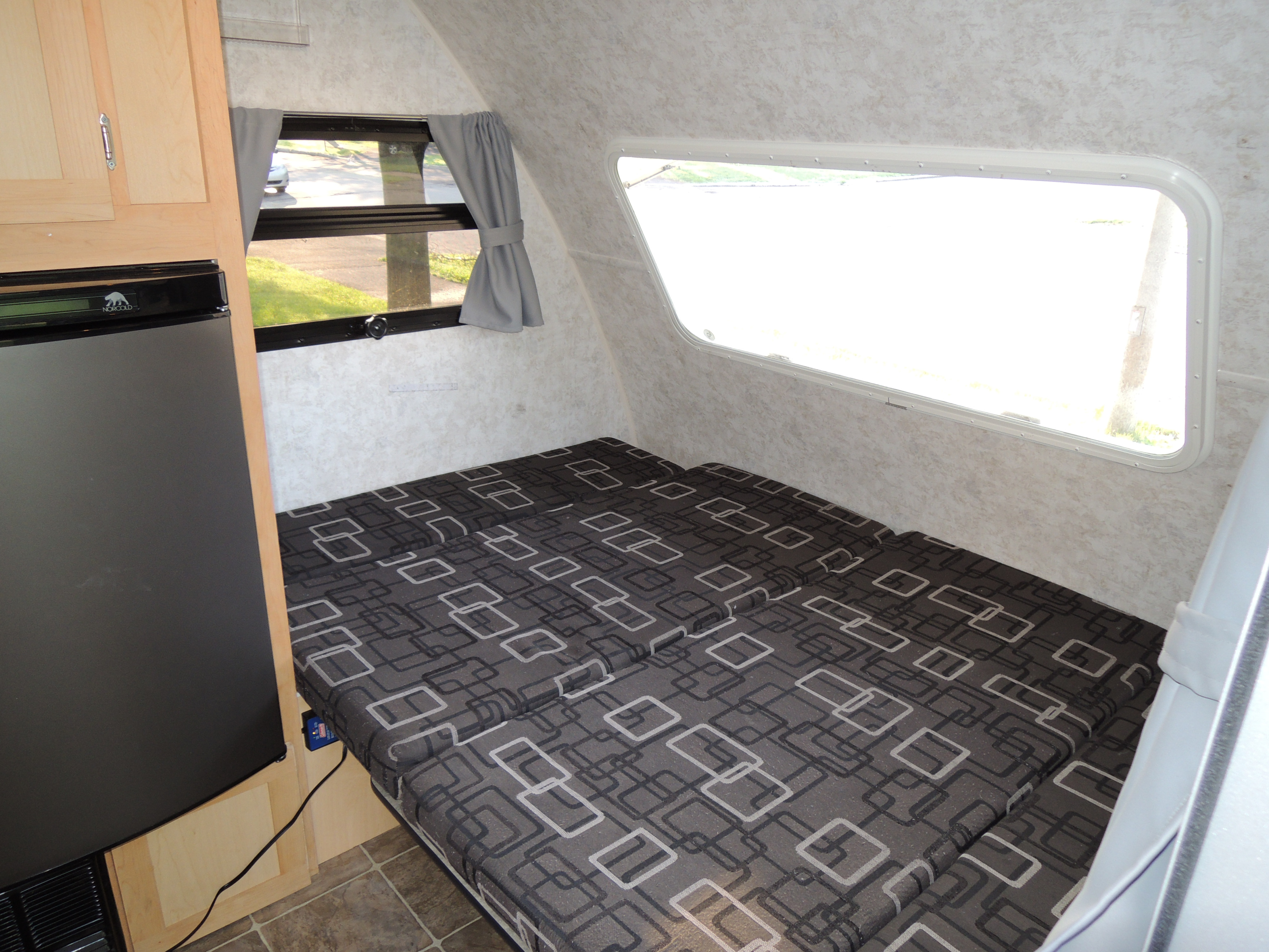 Inside this RV rental: a patterned bed, Norcold refrigerator, and bright windows illuminate this compact camper space.. Prolite Prolite Trailer 2015