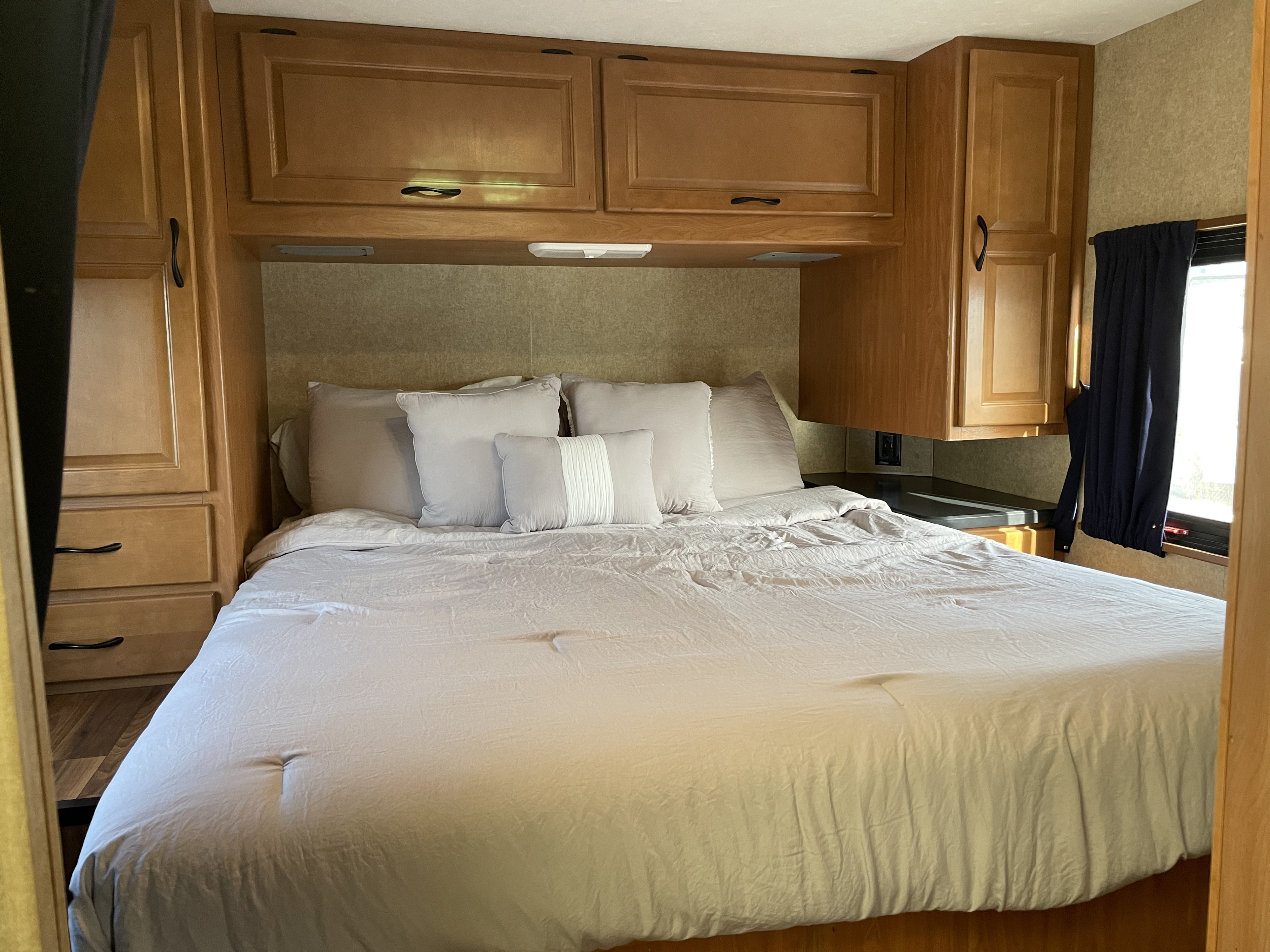 Inside an RV rental, a compact bedroom features a bed with neutral linens, built-in wooden storage, and a small window.. Thor Motor Coach Four Winds Majestic 2016