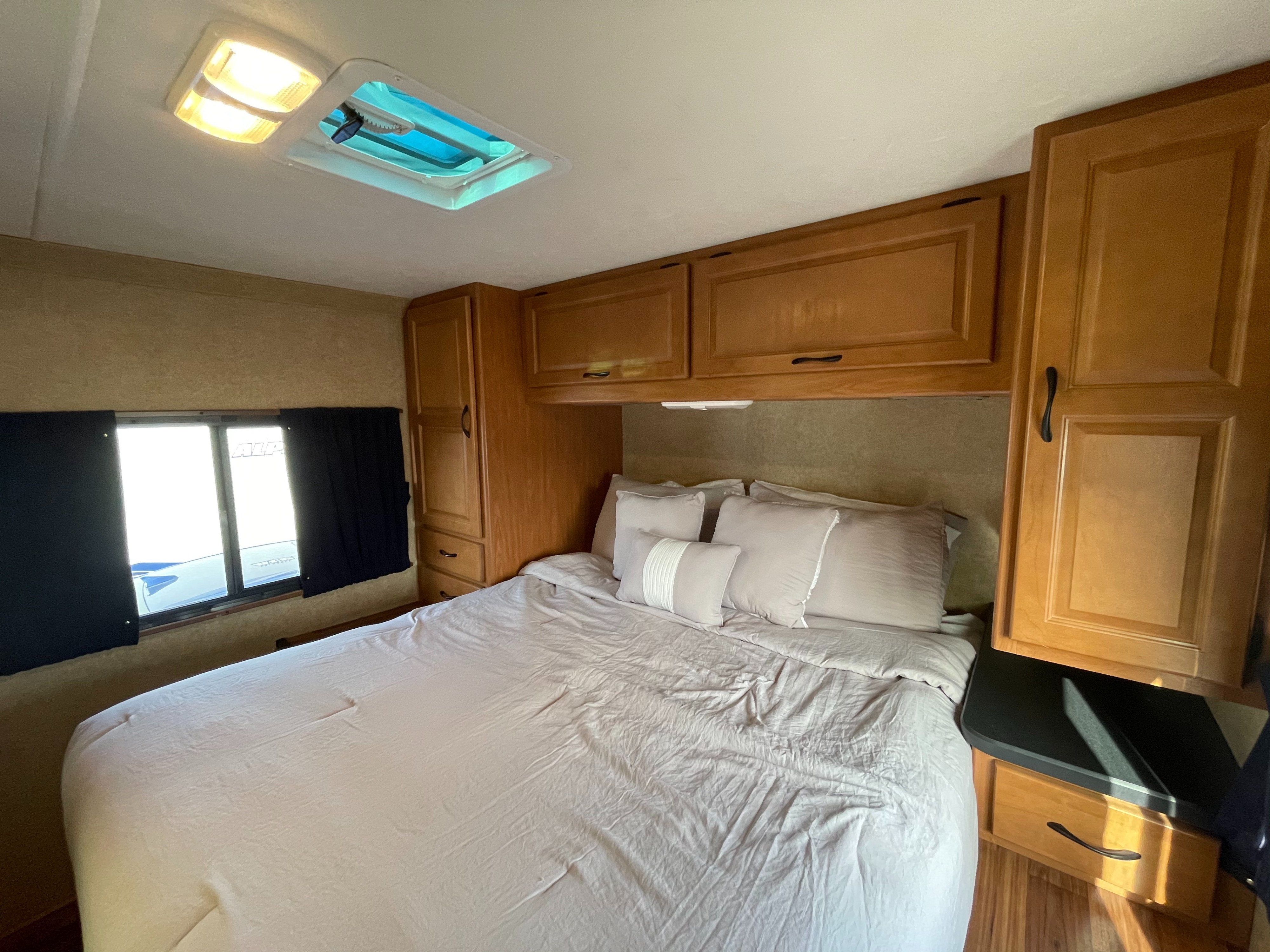 Spacious RV rental bedroom with a comfy bed, wood cabinetry, window, and ceiling skylight for travelers.. Thor Motor Coach Four Winds Majestic 2016