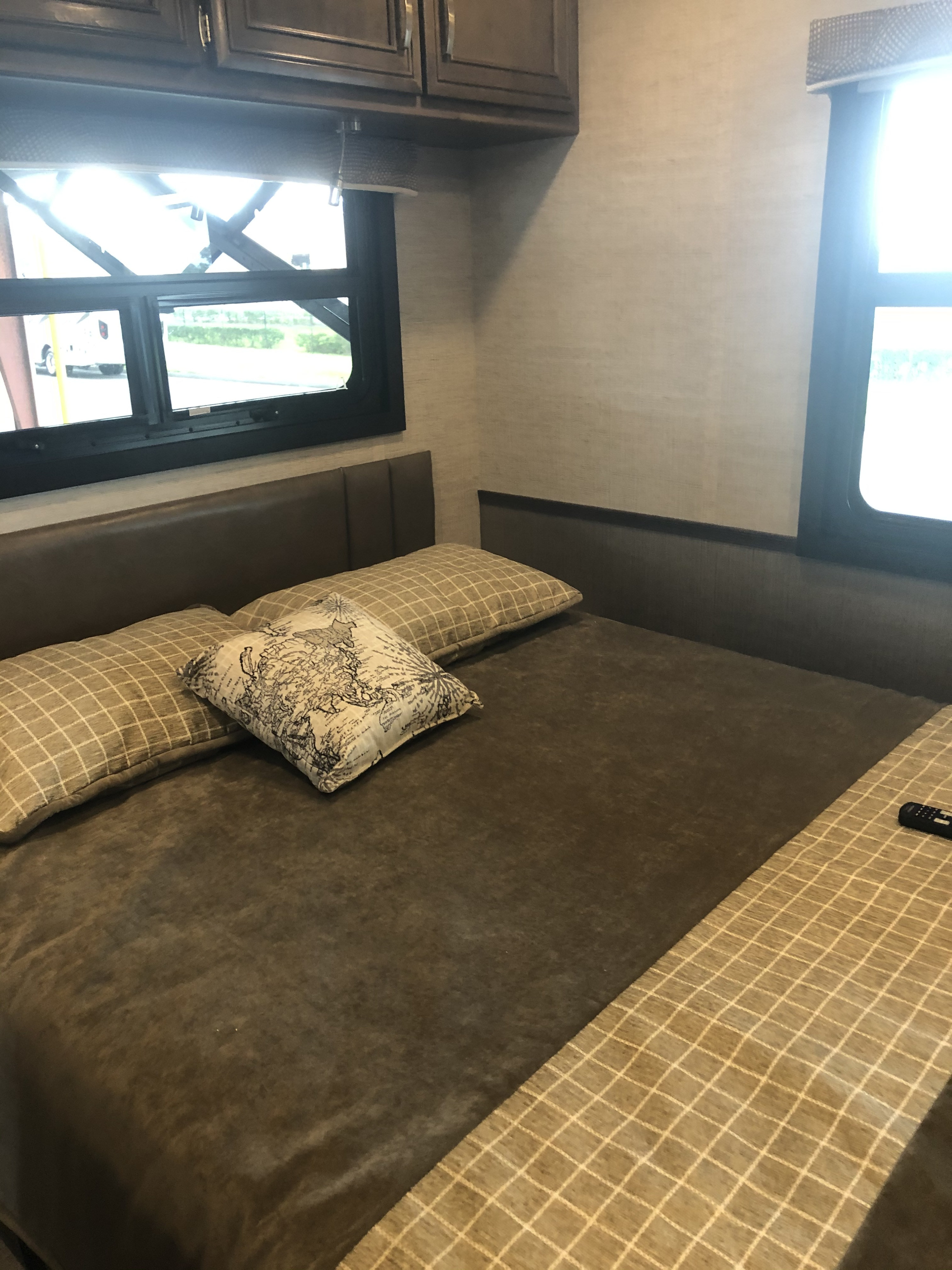 Inside an RV rental: a cozy bedroom featuring a bed with patterned pillows, overhead cabinets, and bright windows.. Entegra Coach Vision 29F 2021