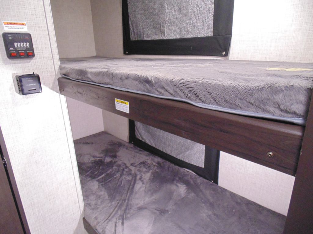 Cozy RV rental bunk beds with fluffy gray mattresses and wall controls, ideal for compact travel lodging.. Keystone RV Bullet Crossfire 2020