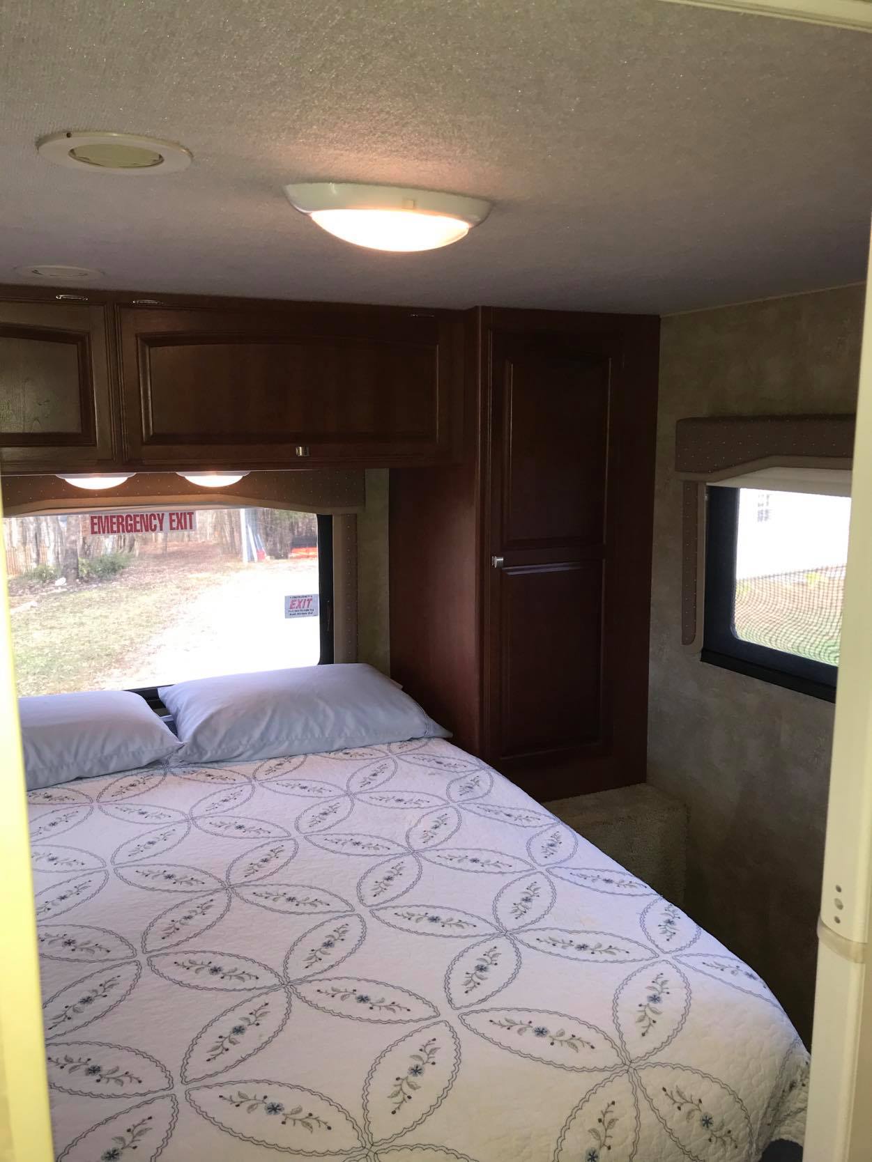 Cozy RV rental bedroom with bed, dark wood cabinets, and an emergency exit window. Ideal for travel accommodations.. Winnebago Chalet 2014