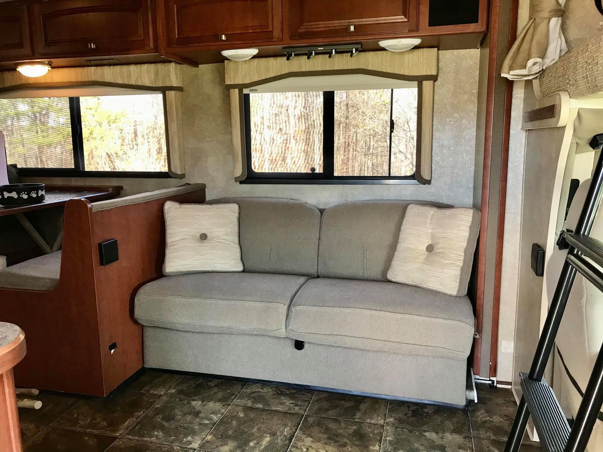 Inside an RV rental: a gray sofa, windows, and a partial view of the dining booth offer a homey living space.. Winnebago Chalet 2014