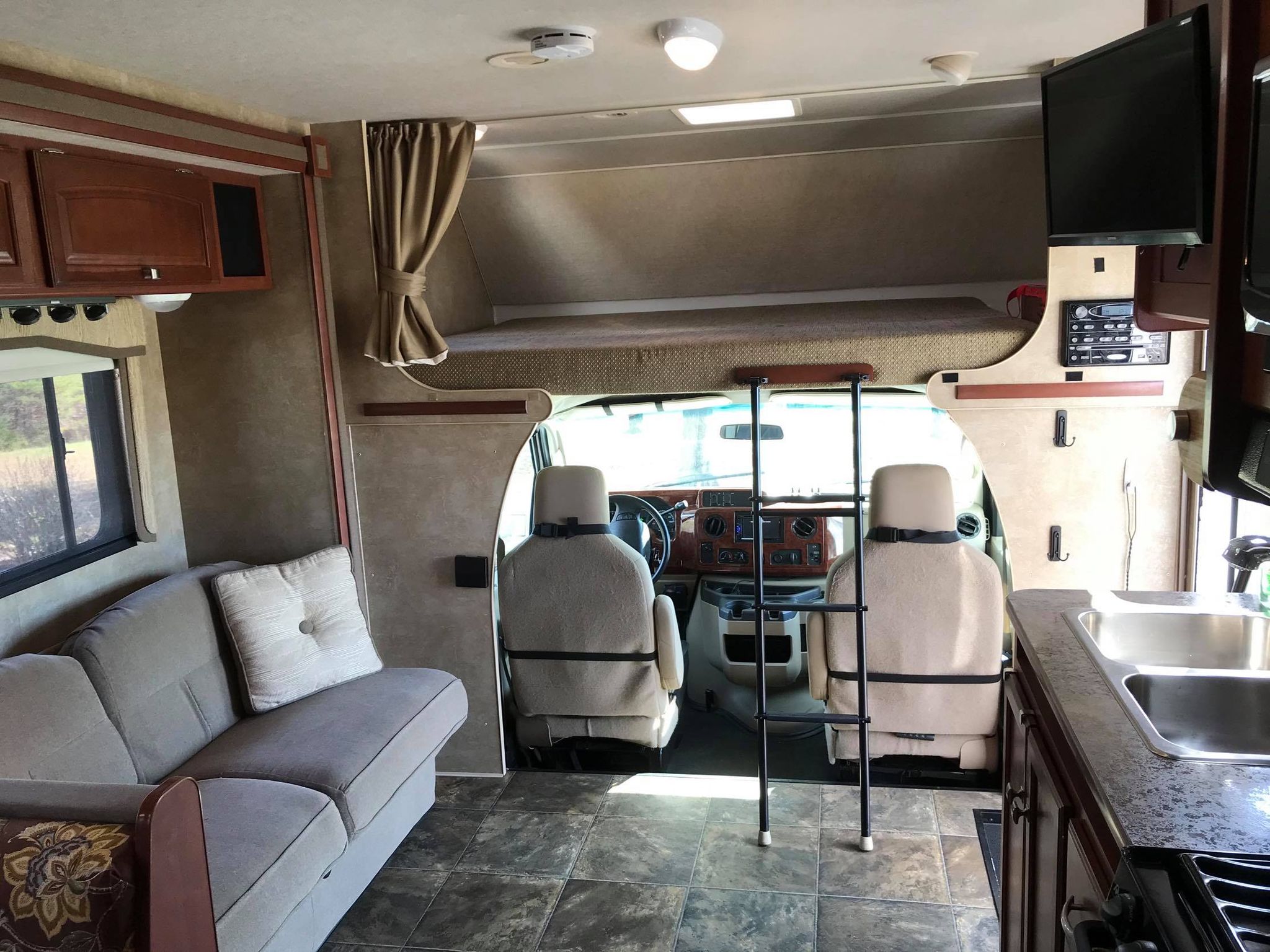 RV rental interior showing a living area with a couch, kitchen, and a cab-over bunk with a ladder.. Winnebago Chalet 2014