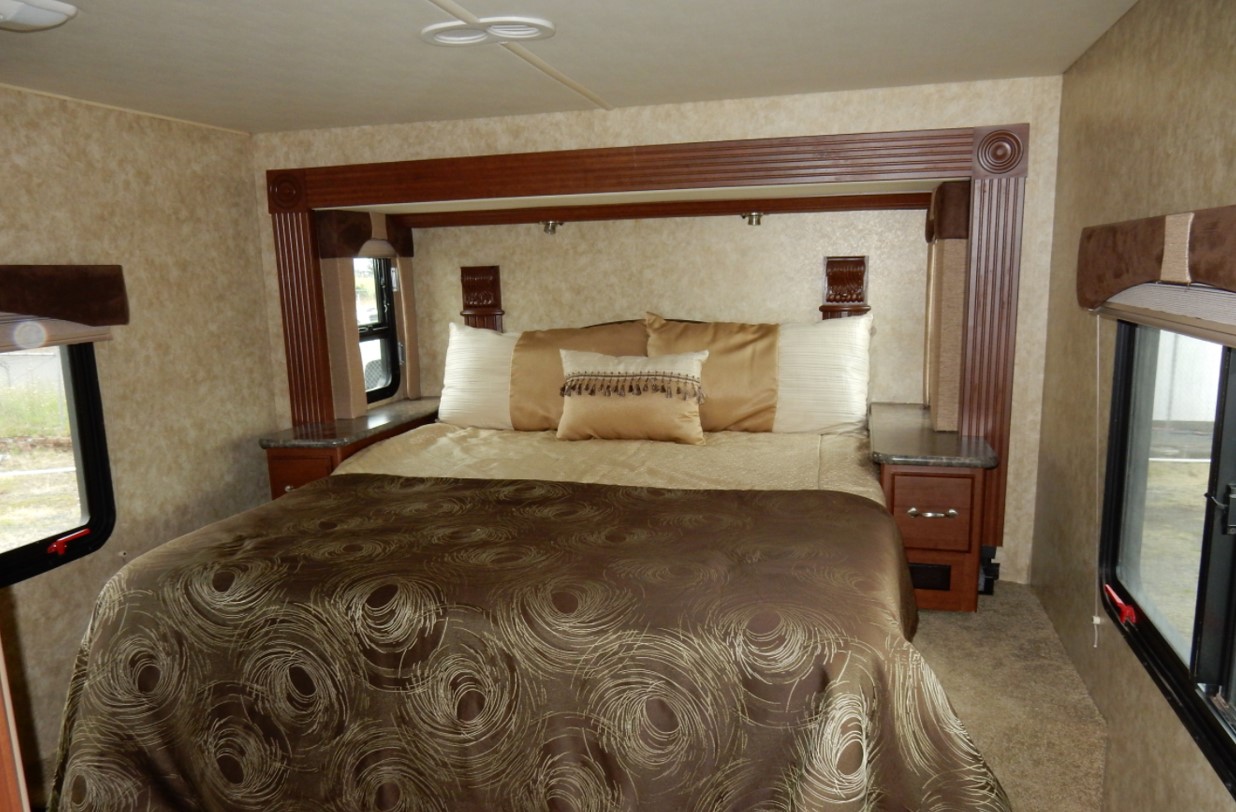 An inviting RV rental bedroom with a large bed, ornate headboard, and windows, offering comfortable sleeping arrangements for your travels.. Fleetwood Storm 2013