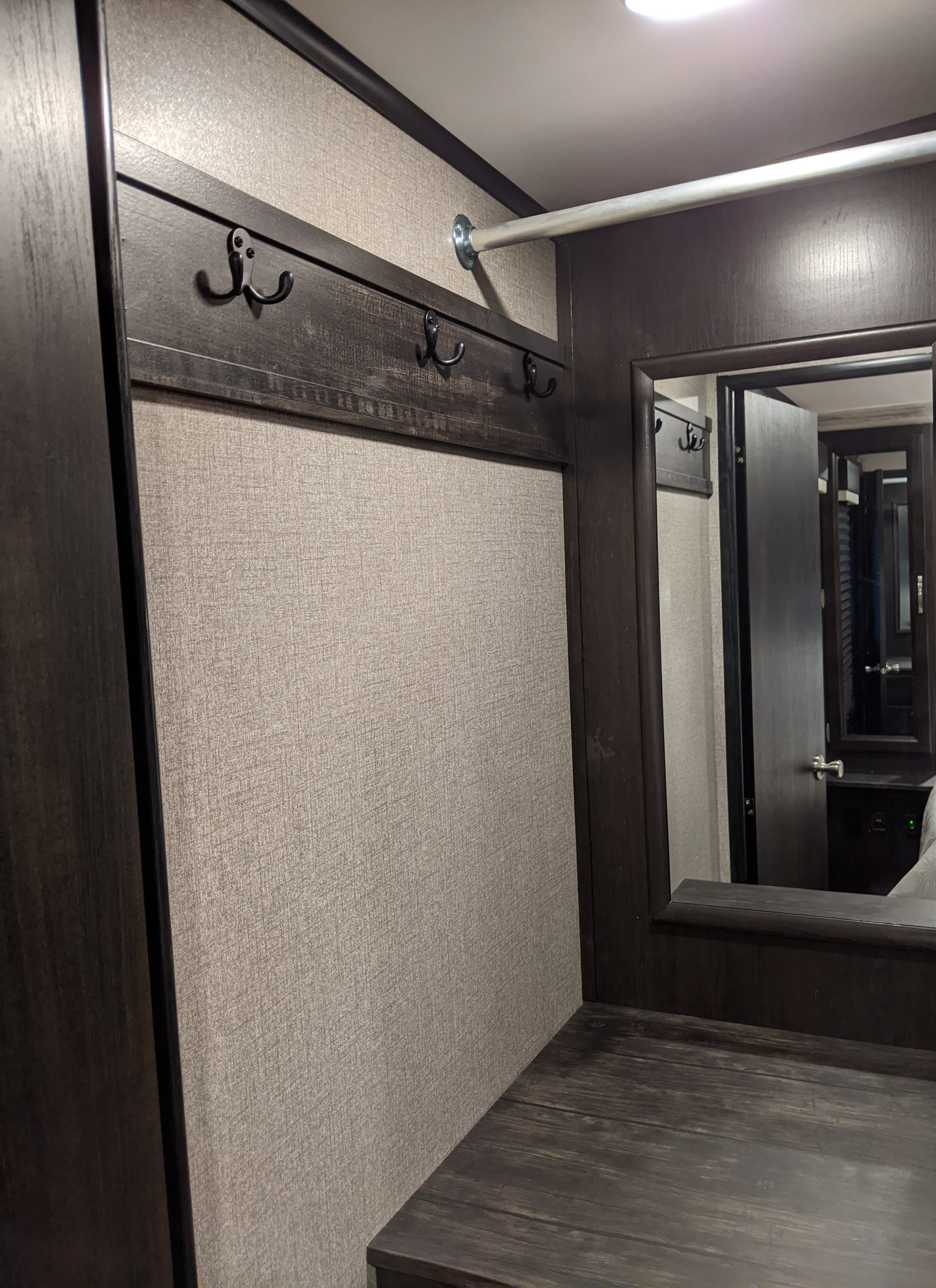 RV rental interior: Features dark wood-look walls, coat hooks, an overhead rod, and a mirror for compact living.. Jayco White Hawk 2021