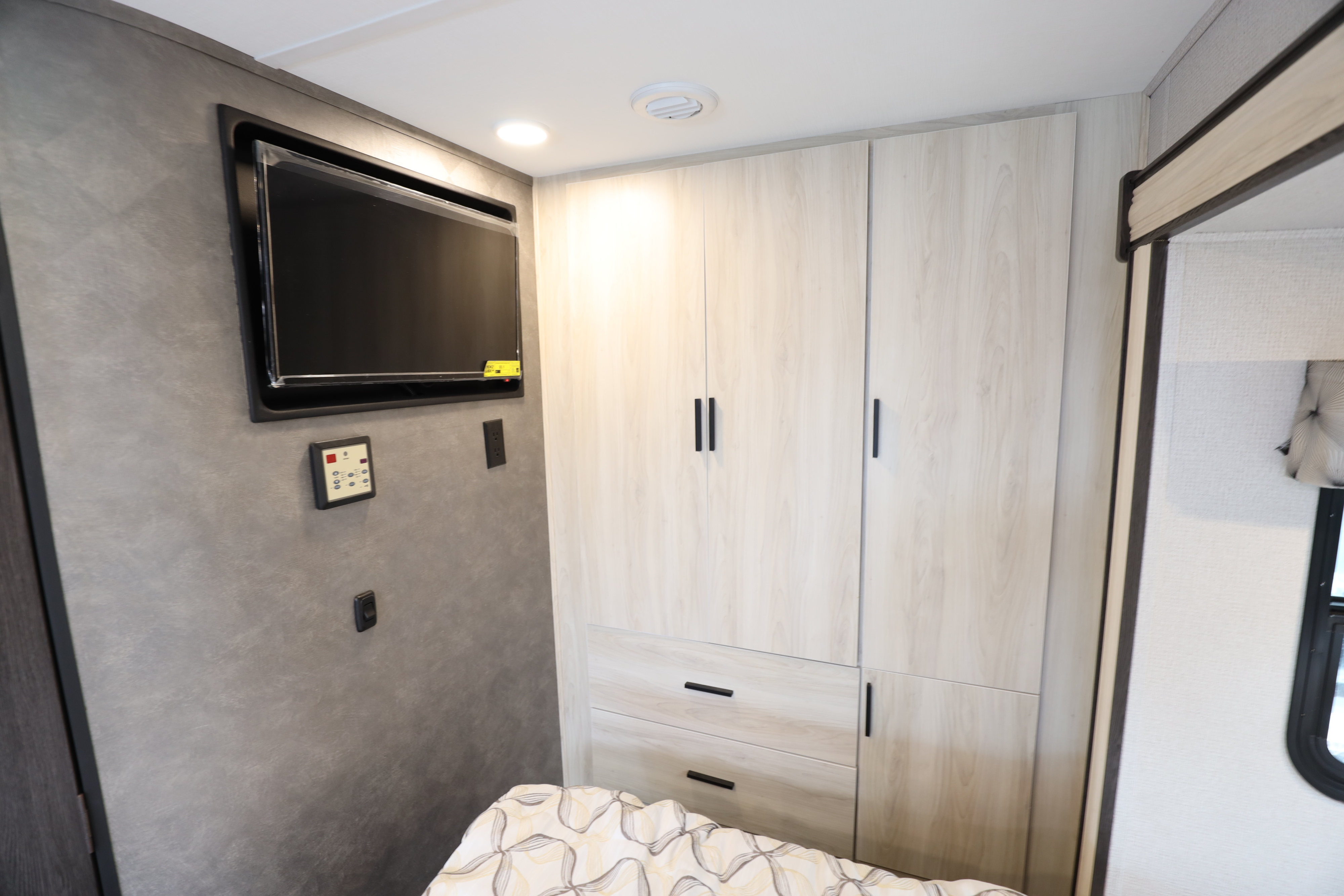 RV rental bedroom interior showing a mounted TV, light wood wardrobe with drawers, and bed.. Classe C mercedes 24 pieds avec extension 2021