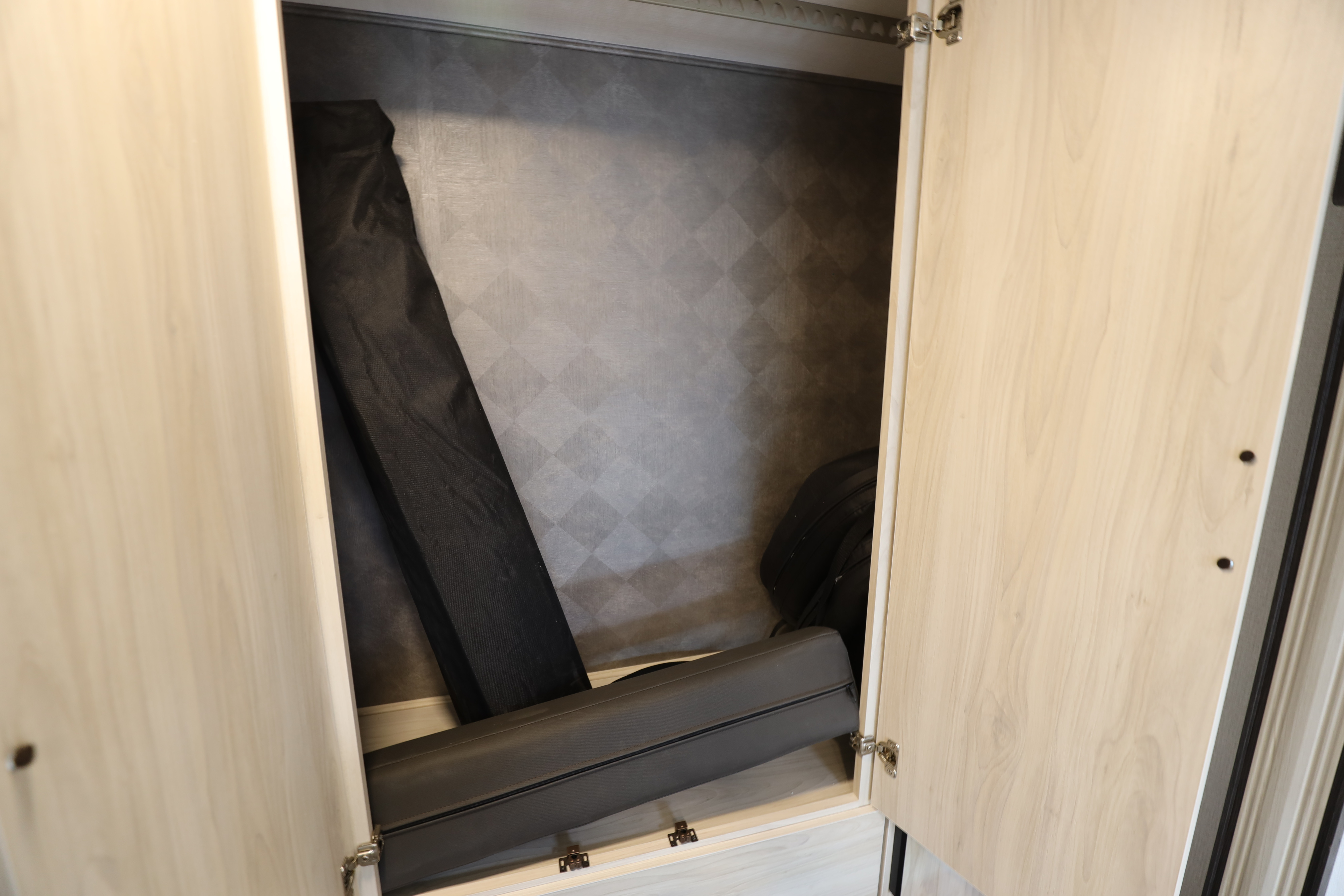 RV rental storage: An open RV closet reveals a long black bag and a dark gray zippered cushion or mattress.. Classe C mercedes 24 pieds avec extension 2021