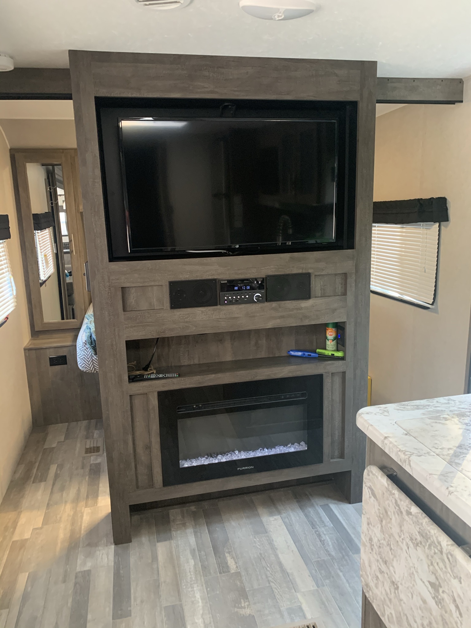 Modern RV rental interior featuring an entertainment center with a TV, stereo, and electric fireplace, complemented by sleek grey flooring.. Forest River Vibe 2021