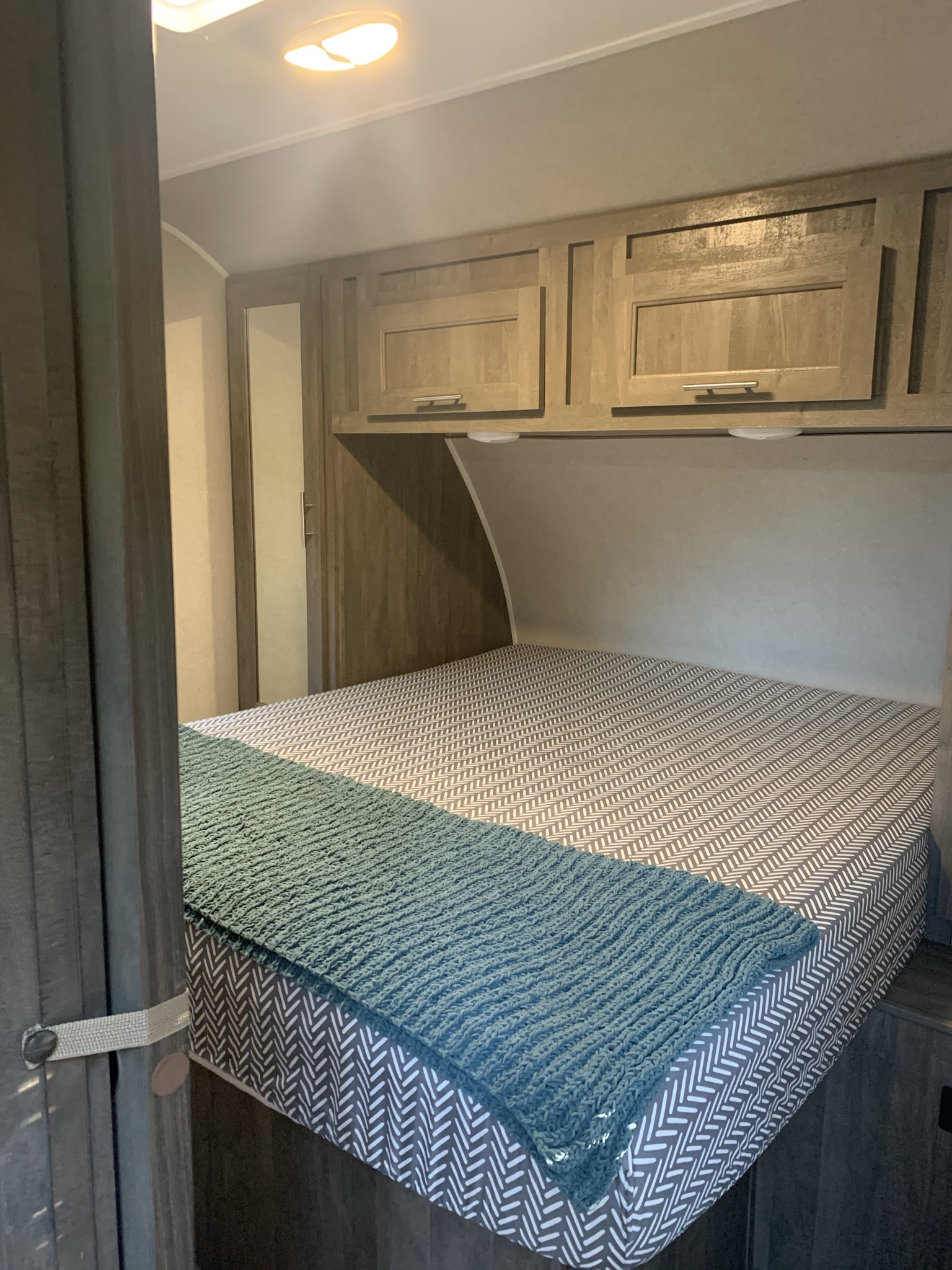RV rental interior: well-lit bedroom with bed, herringbone mattress, teal blanket, and wood cabinets.. Forest River Vibe 2021
