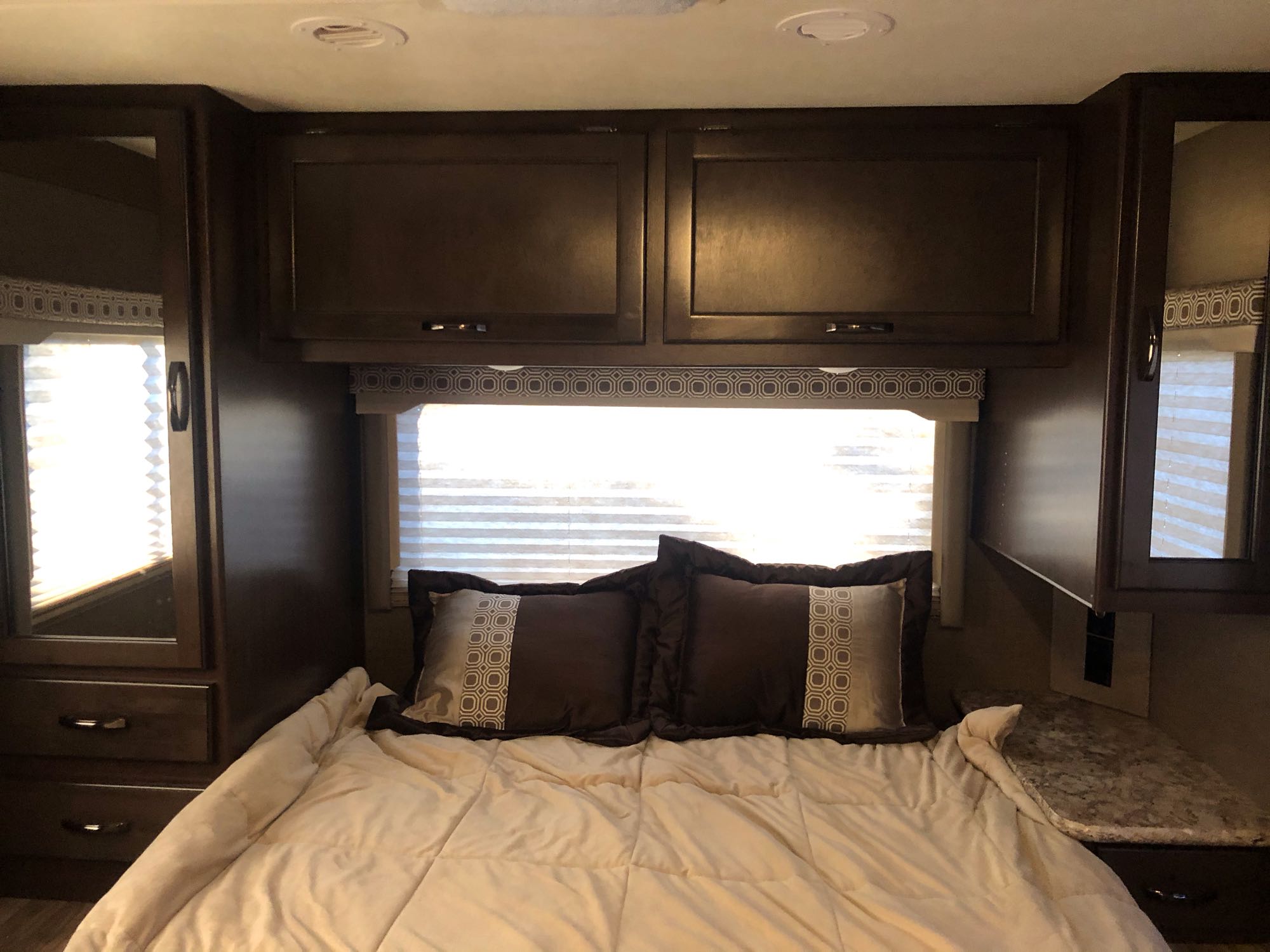 Cozy RV rental bedroom featuring a bed, overhead cabinets, and side storage with mirrors, perfect for travel.. Thor Four Winds 2020