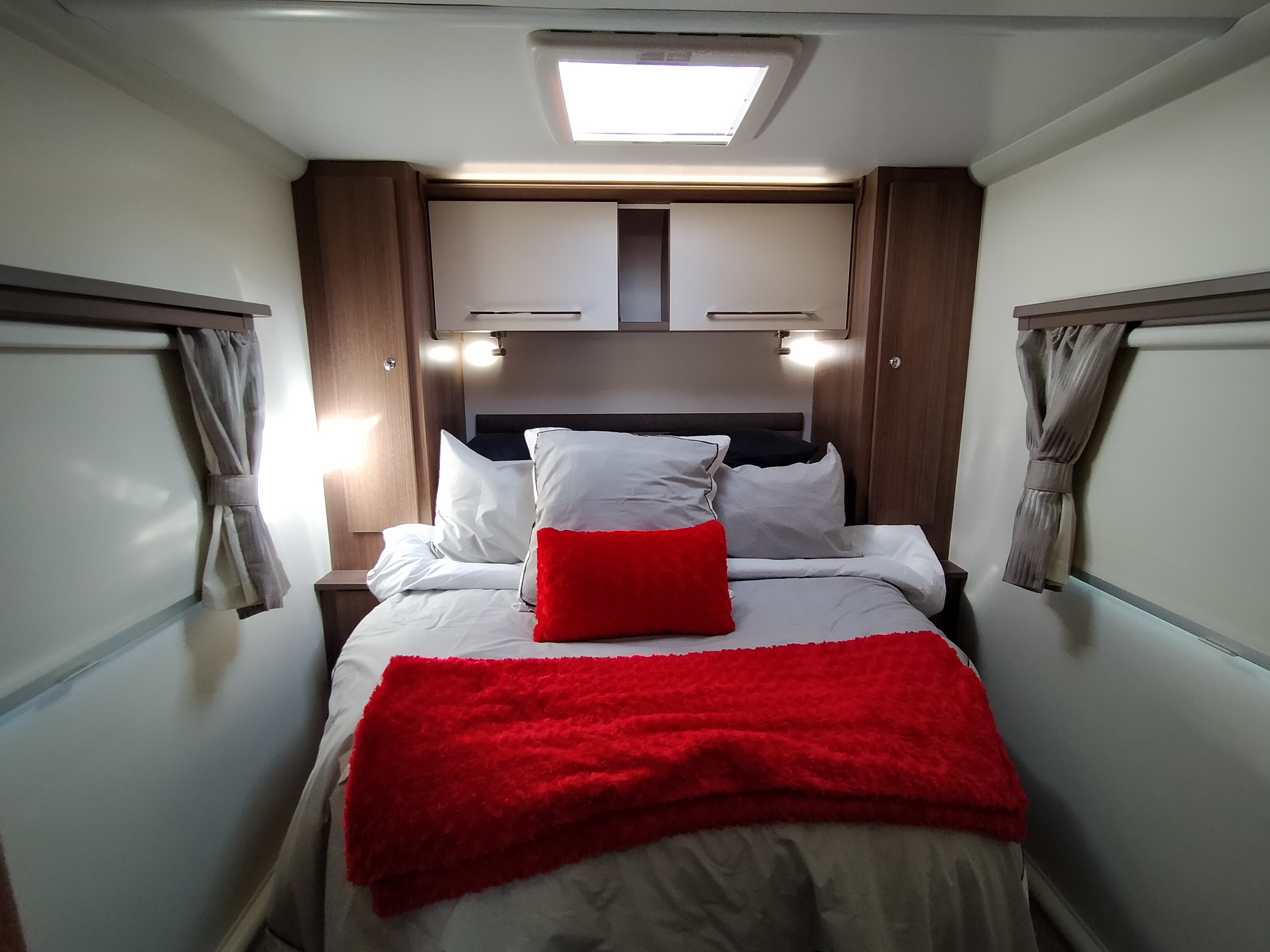 Cozy RV rental bedroom with a queen bed, bright red accents, built-in cabinets, and soft ambient lighting for comfort.. Bailey Pheonix 640 2022