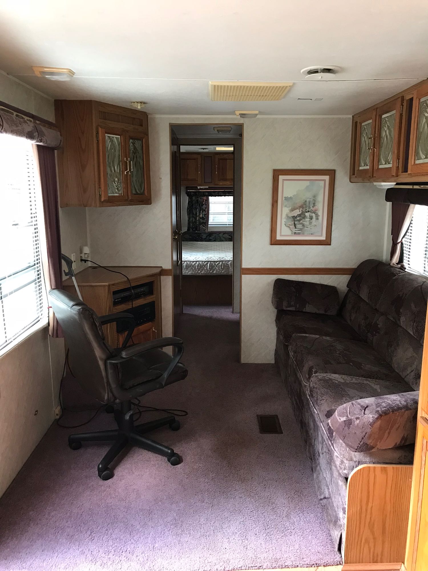 Inside this RV rental: a living area with a brown couch, office chair, wooden cabinets, and a view into the bedroom. Purple carpet.. Jayco Jay Series 1996