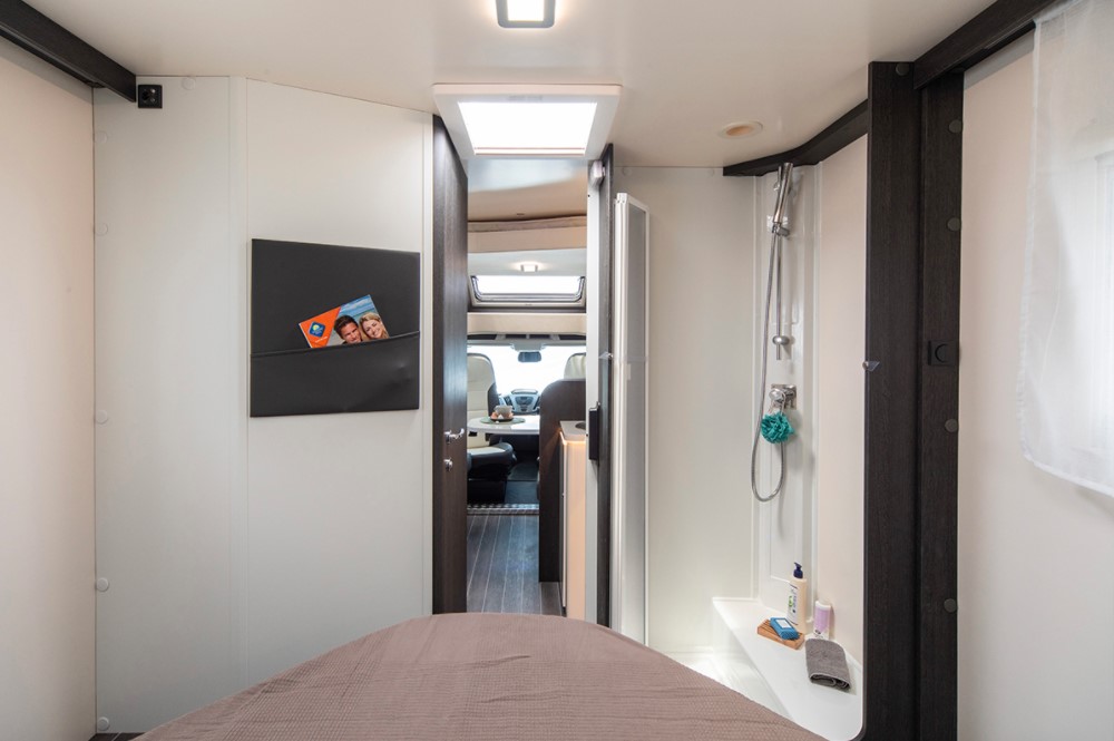 Experience an RV rental! This cozy RV interior features a bed, compact shower, and a connected living area towards the driver's cab.. Rollerteam Zefiro 696 2025