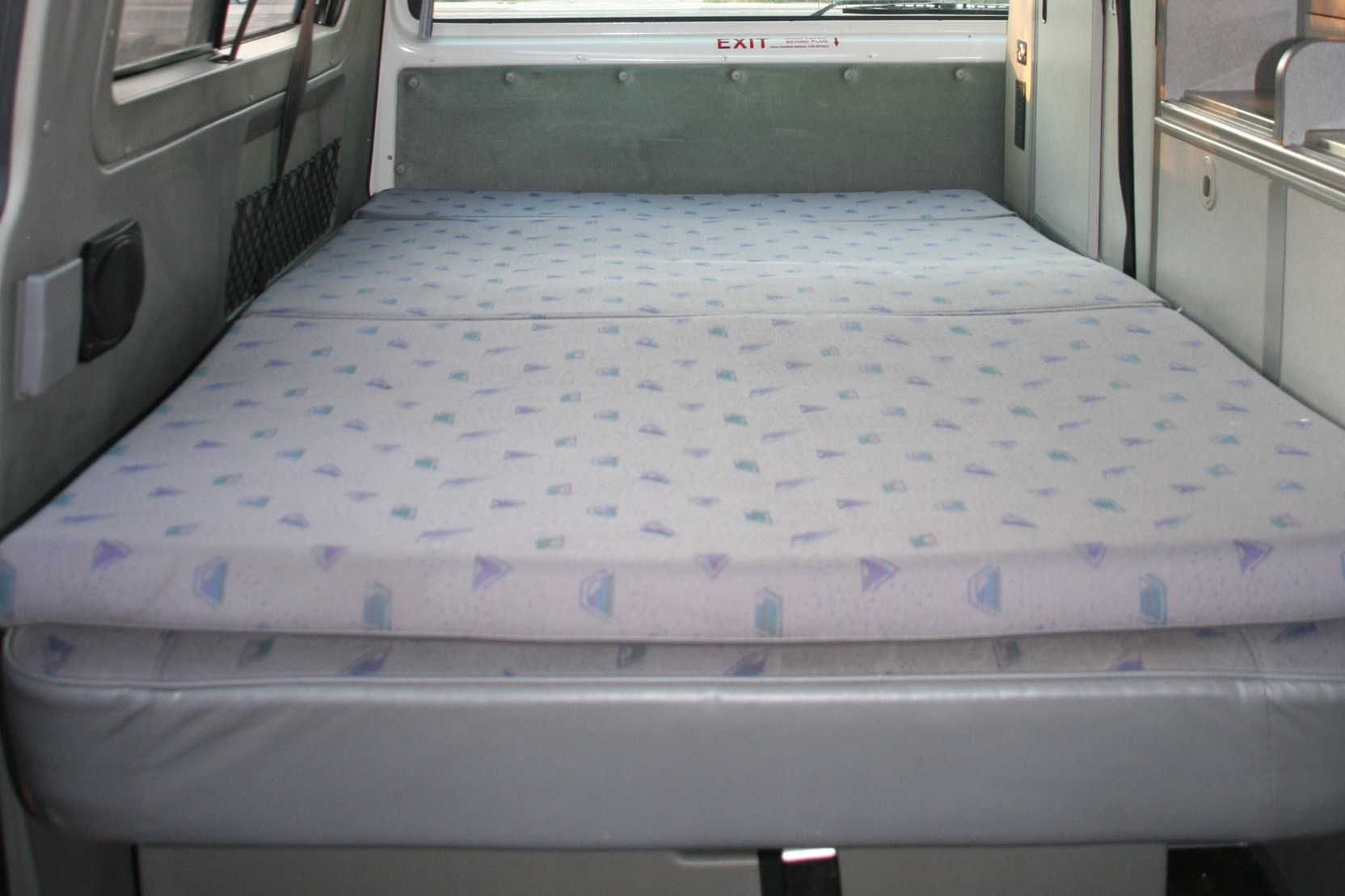 RV rental interior featuring a neatly made bed with patterned cushions on a grey base, ideal for compact travel.. Volkswagen Other 1999