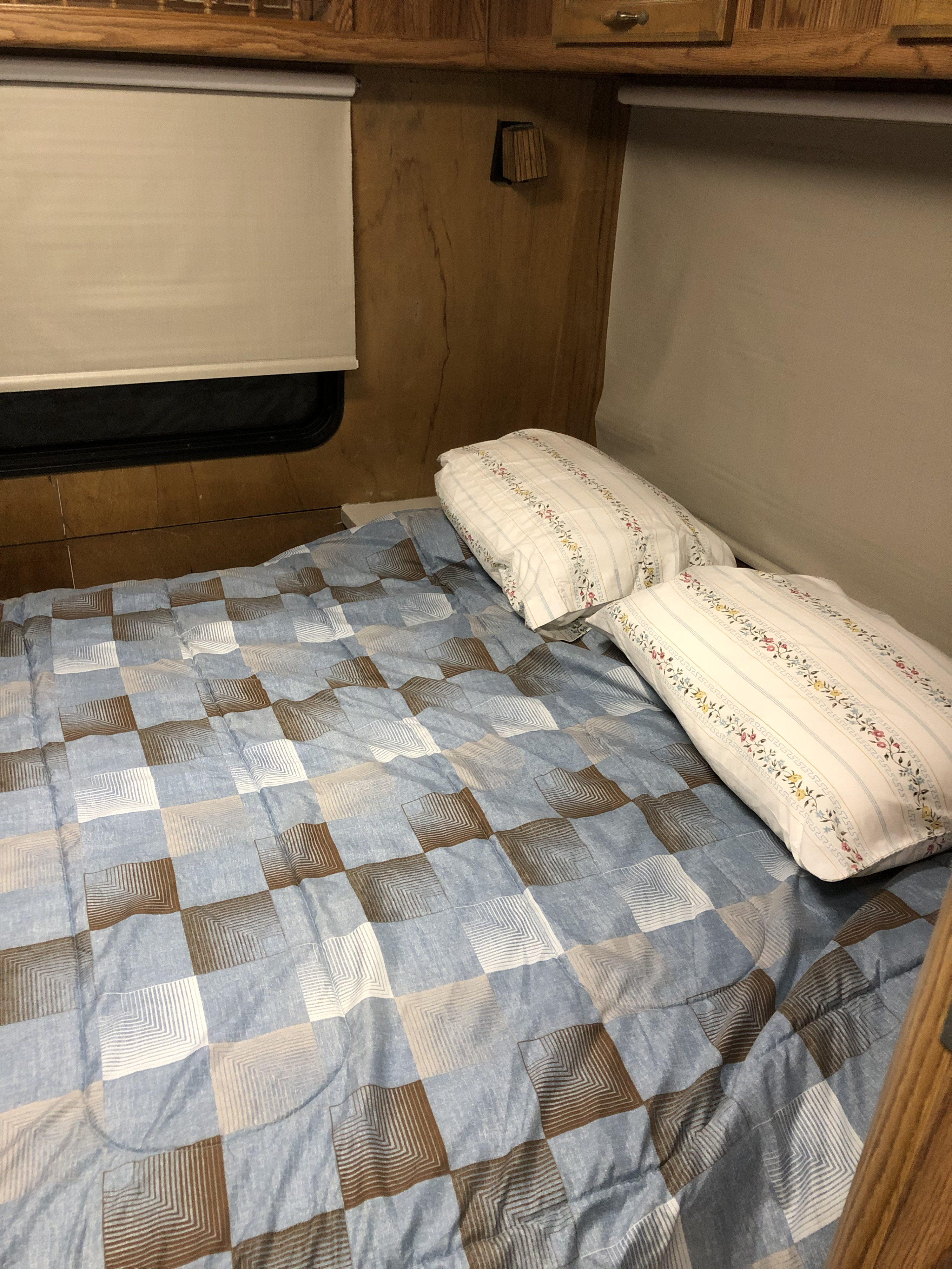 Inside an RV rental, a comfy bed with a blue, brown, & white comforter, and patterned pillows.. National Dolphin 1987