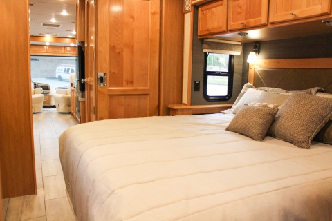 Spacious RV rental bedroom with warm wood interiors, a comfortable bed, and a clear view to the front cabin area.. Tiffin Motorhomes Allegro Red 2021