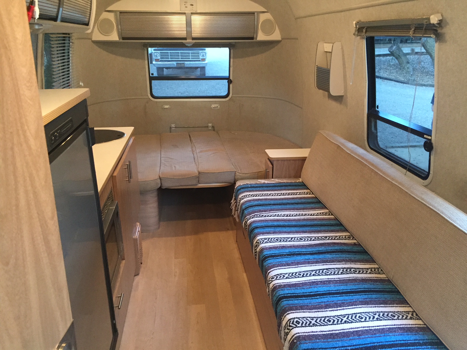 Compact RV rental interior featuring a kitchen, convertible bed, and cozy bench seating with a vibrant blanket.. Airstream Safari 2008