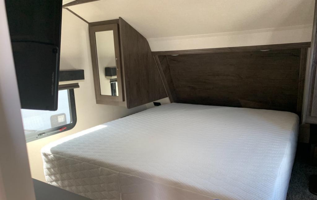 RV rental bedroom with a comfy white mattress, wood headboard, mirrored cabinet, and window for natural light.. Forest River Salem Hemisphere GLX 2019