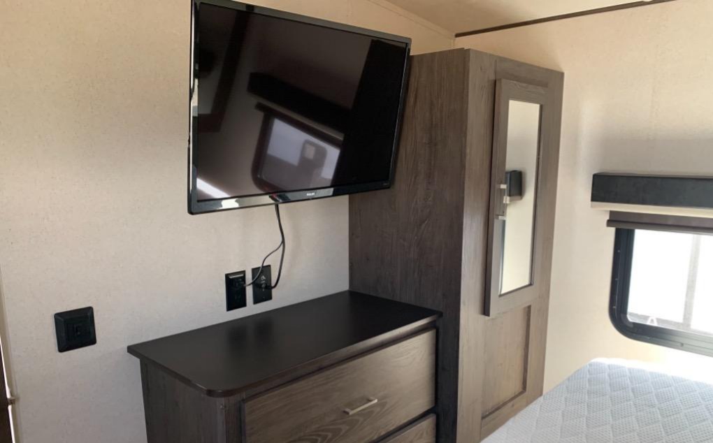 RV rental bedroom: wall-mounted TV, dark wood dresser with outlets, mirrored closet, window, and bed for your travels.. Forest River Salem Hemisphere GLX 2019