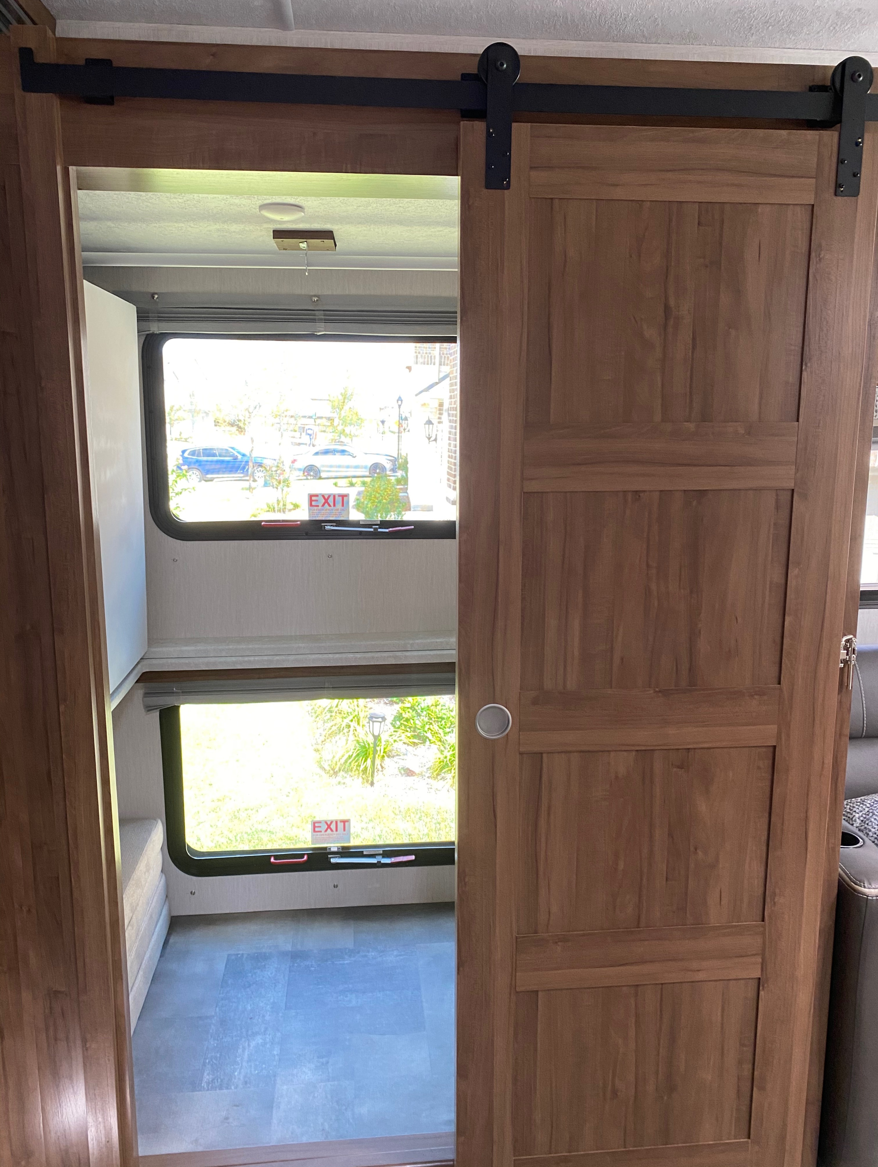 RV rental interior: a stylish sliding barn door opens to a cozy bunk bed area with dual windows, marked 'EXIT'.. Coachmen Mirada 2021
