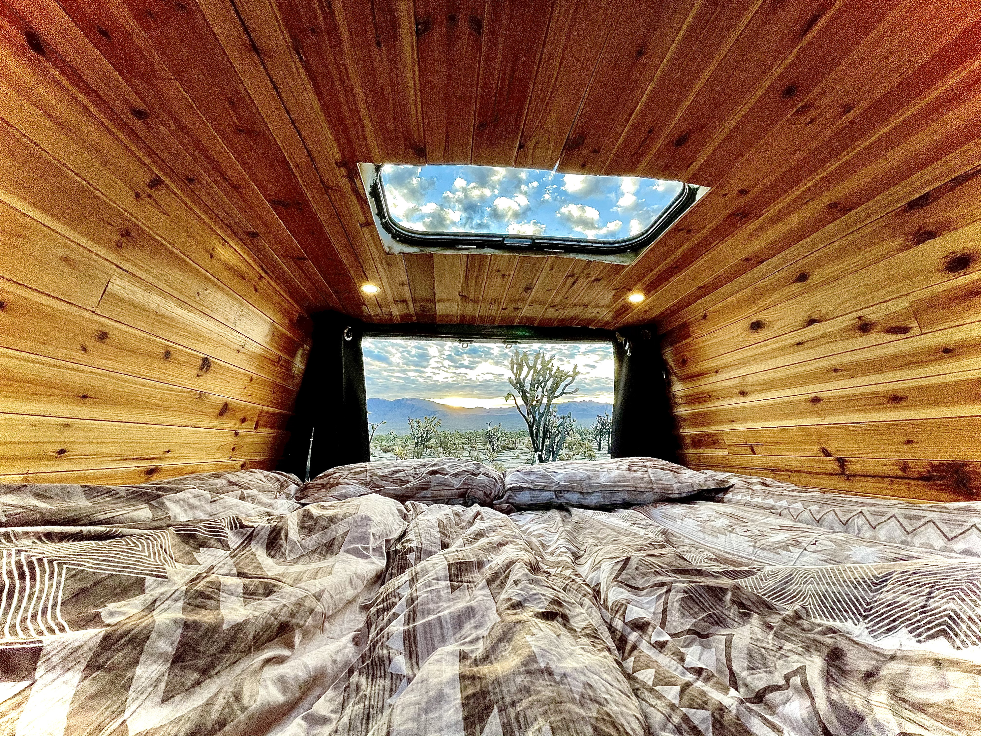 Cozy RV rental interior with bed and wood paneling, offering stunning desert sunset views and a sky through the roof.. Mercedes-benz 4x4 Sprinter mwb 2019