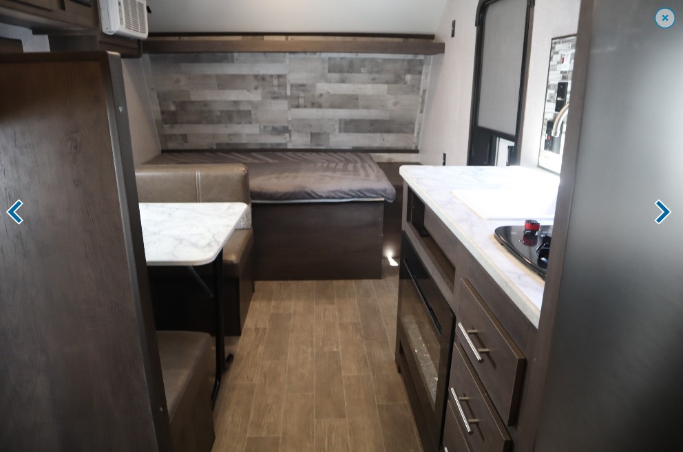This RV rental interior showcases a cozy living space with a dining booth, bed, and compact kitchen counter.. Dutchmen Coleman 2020
