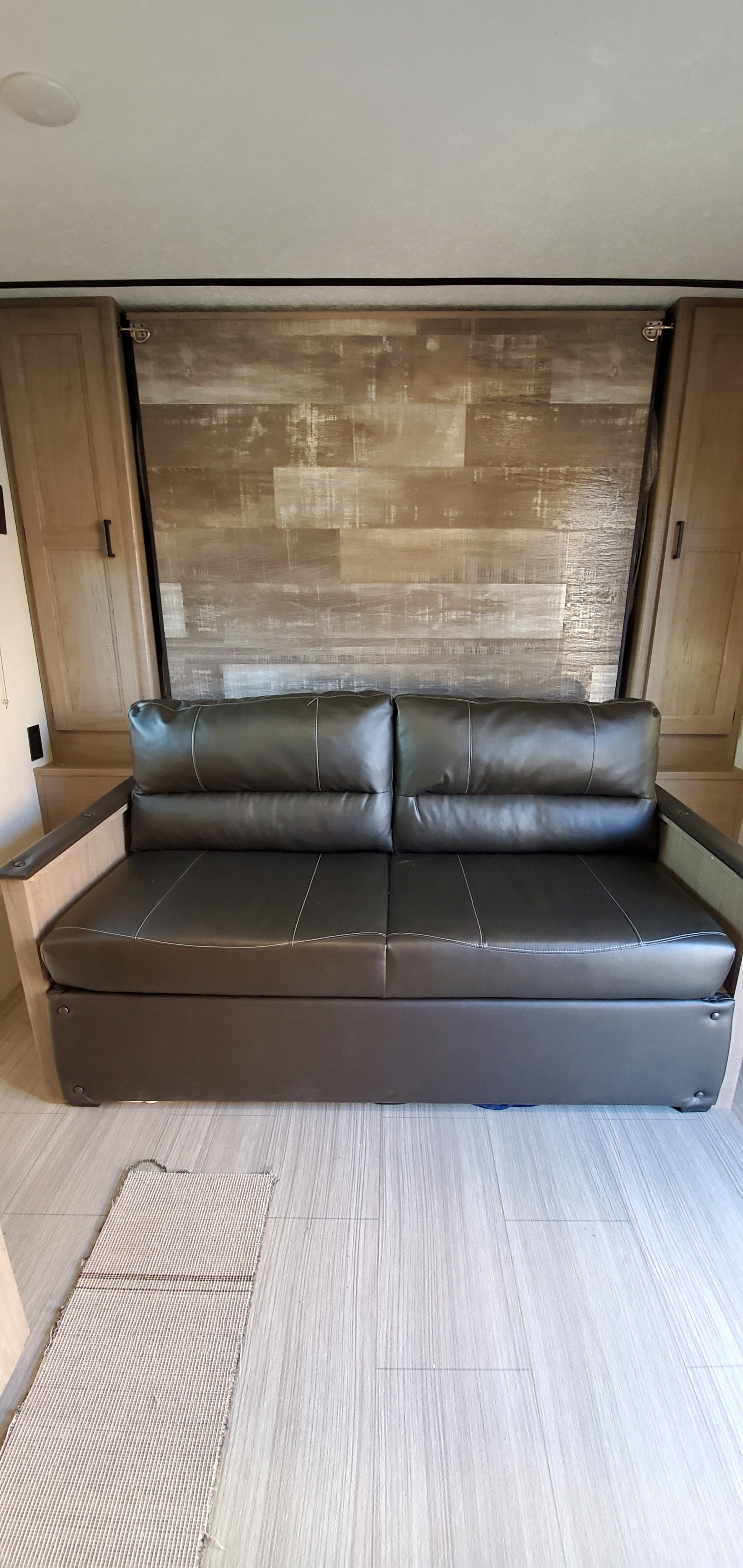 Cozy RV rental interior featuring a dark leather sofa against a rustic wood-paneled wall, flanked by light wooden cabinets.. Keystone RV Hideout 2021