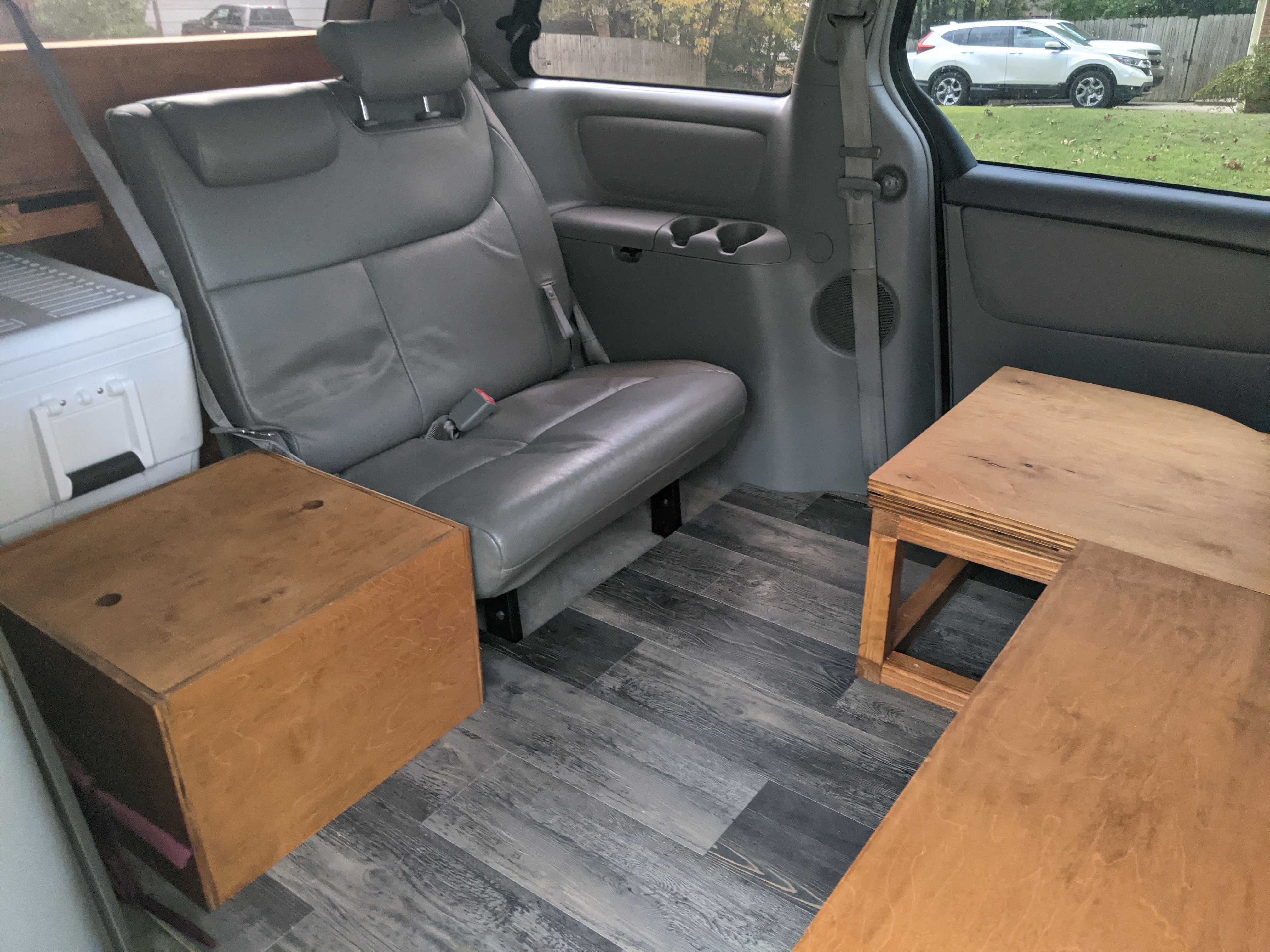 RV rental minivan interior showing a rear seat, white cooler, and wooden storage on a gray plank floor.. Toyota Other 2007