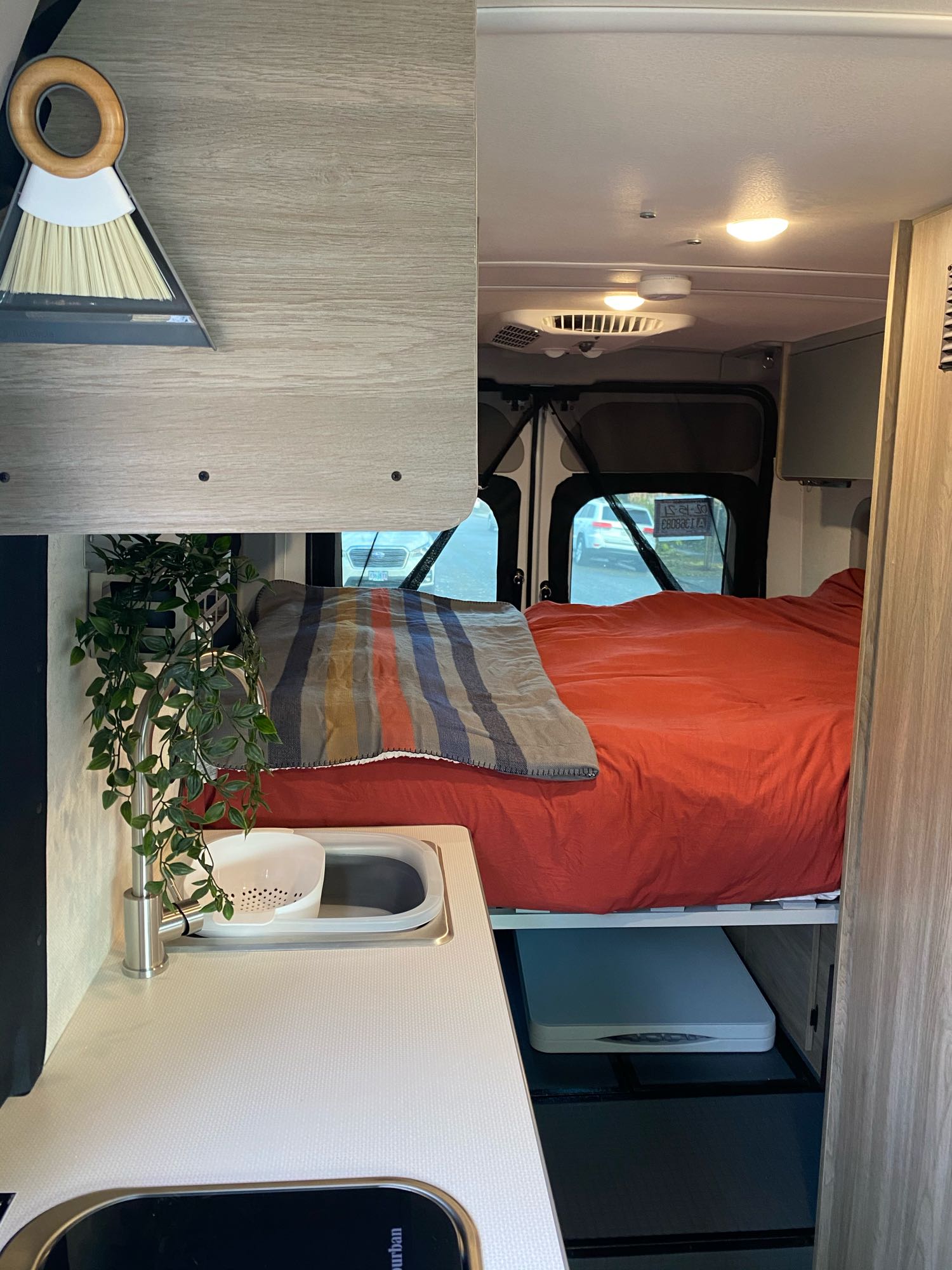 Inside a functional RV rental: comfy bed, compact kitchen with sink, and hanging plant. Includes a broom and dustpan.. Winnebago Winnebago 2021