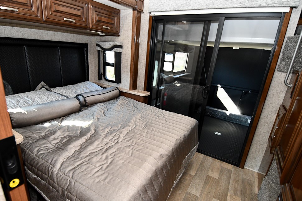 Comfortable RV rental bedroom with a large bed, cabinets, and a sliding door leading to a garage area. Ideal for travel.. Ford Other 2019