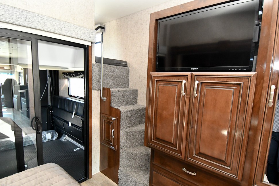 Inside an RV rental: carpeted stairs, TV cabinet, and sliding door to the rear garage/living space.. Ford Other 2019