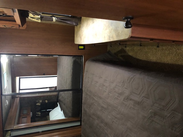 RV rental interior: A cozy bedroom with a large bed, mirrored wall reflecting a window and sleeping area.. Dutchmen Denali 2014