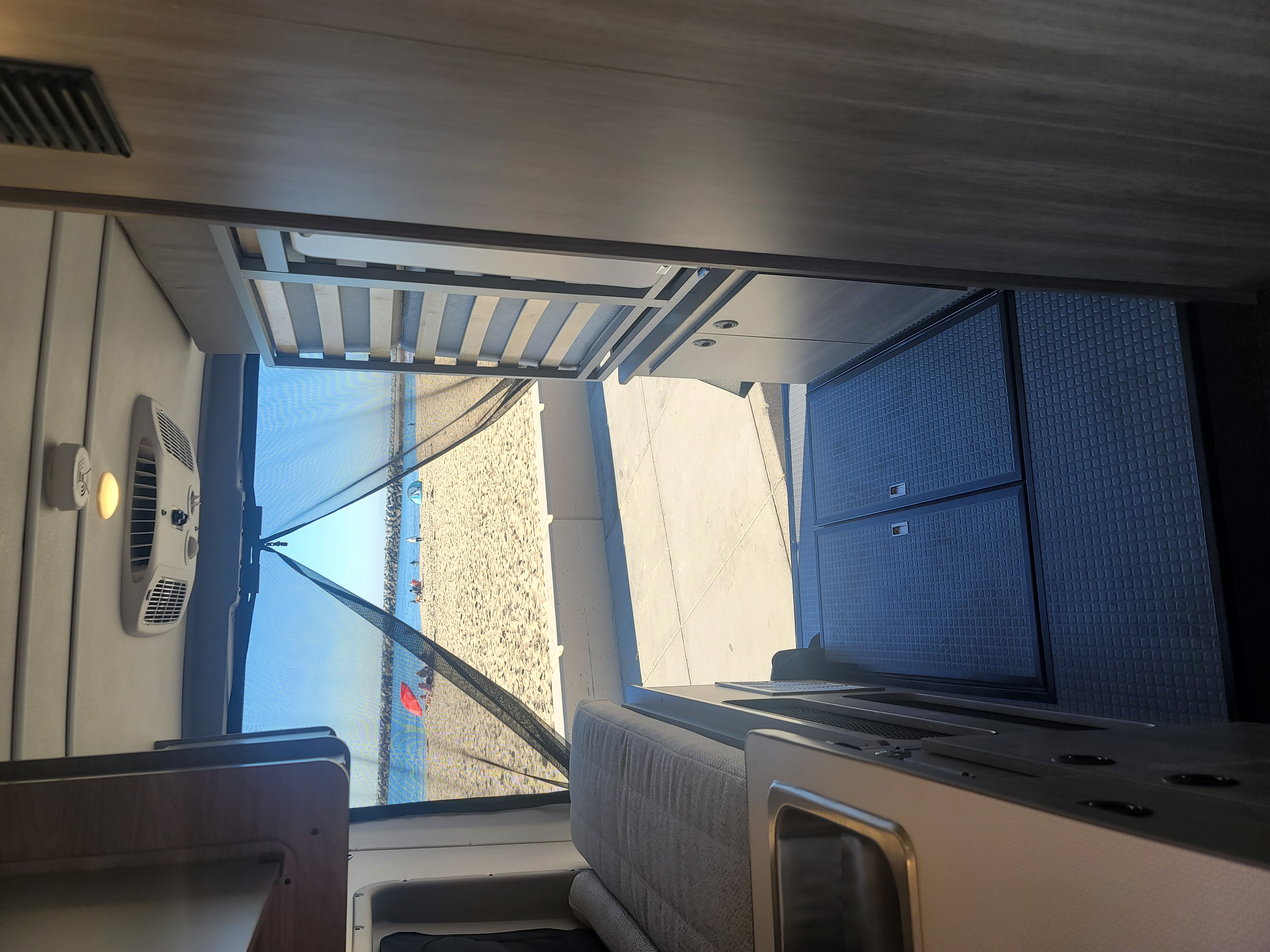 Enjoying the ultimate rv rental view! Inside a camper van, looking out through a mesh screen to a sandy beach and ocean.. Winnebago Solis 59PX 2021