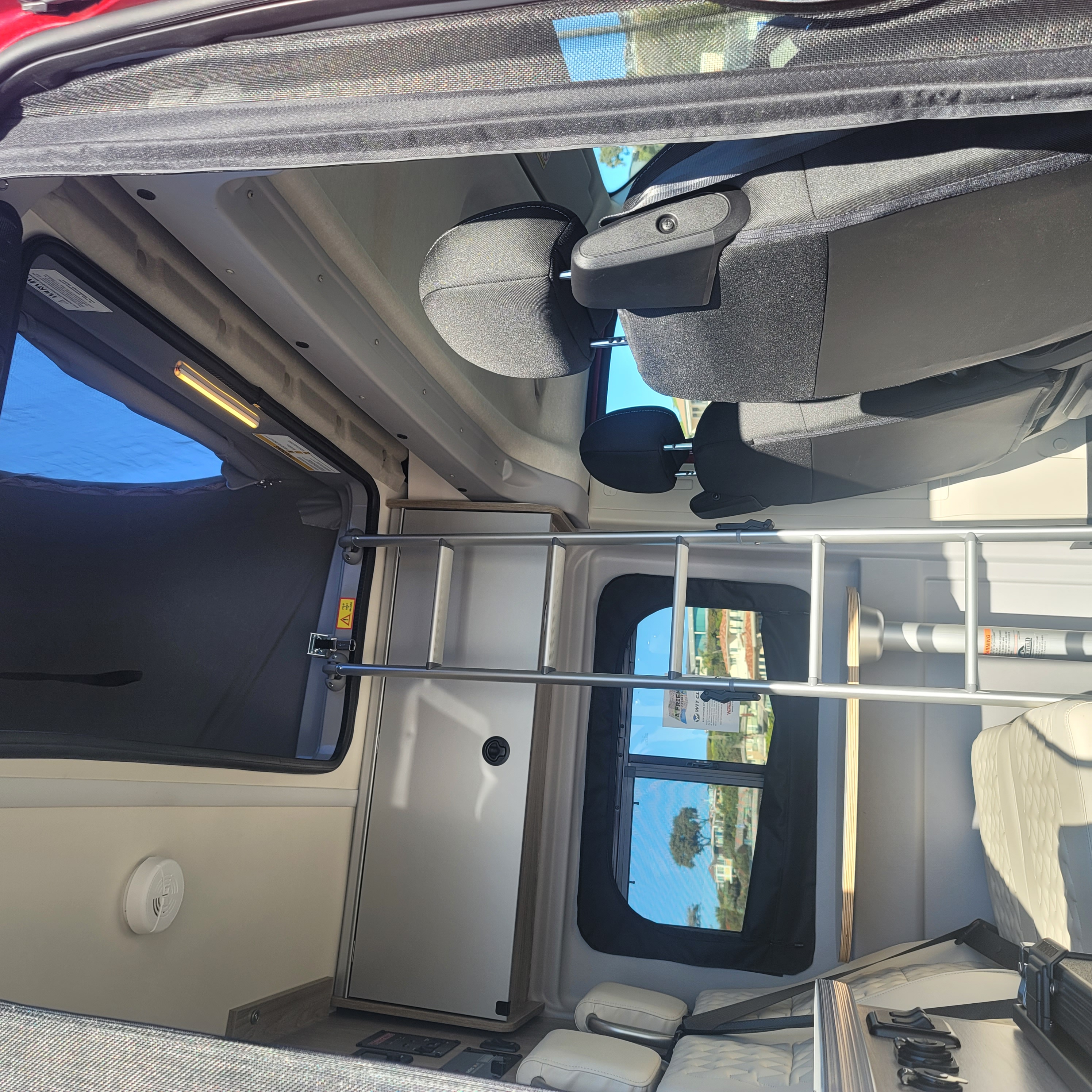 Inside an RV rental: a modern camper van interior with front seats, a ladder to a bunk, windows, and storage.. Winnebago Solis 2021