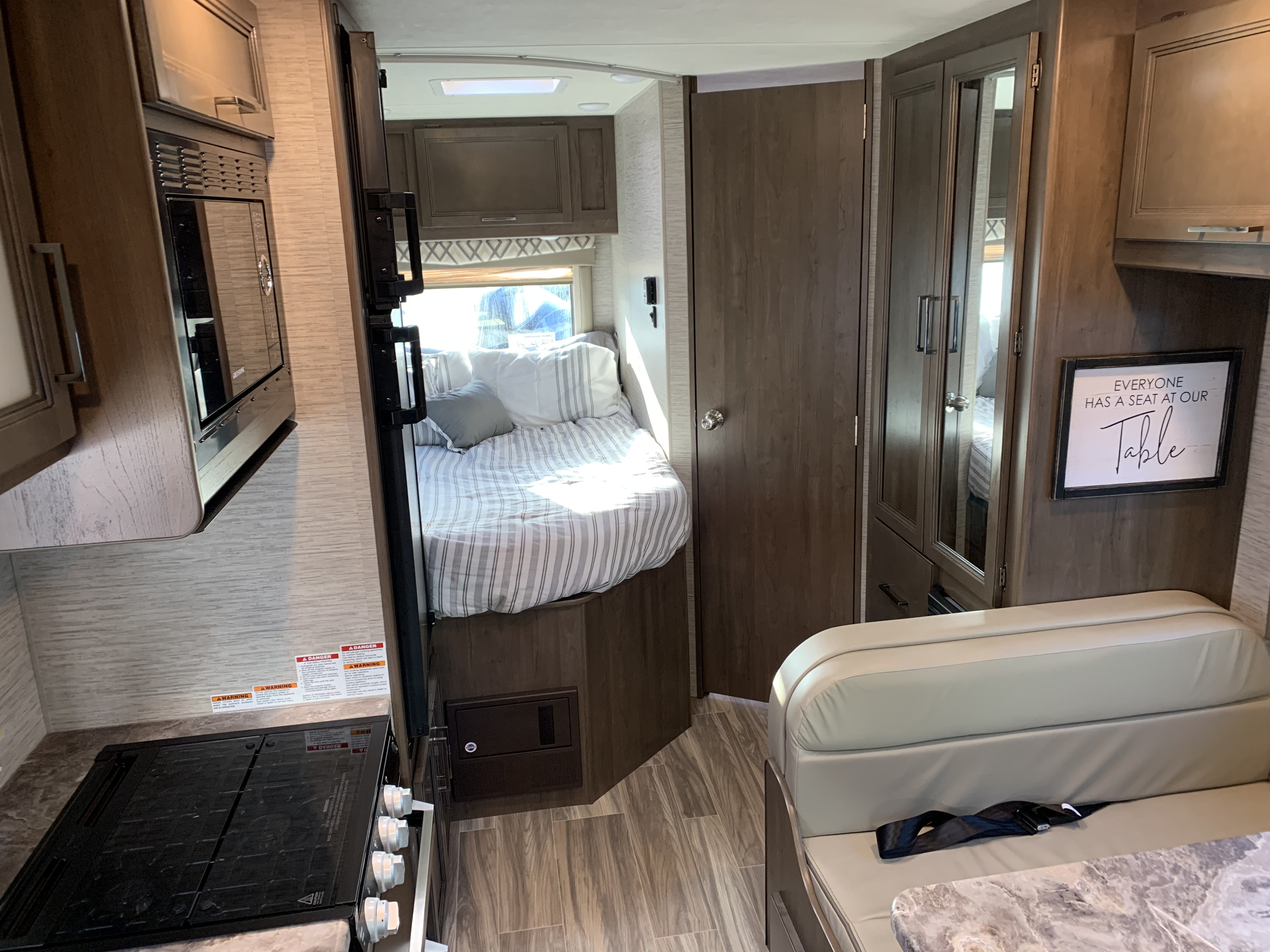 View of a modern RV rental interior showing a compact kitchen, bed, and dinette area.. Thor Motor Coach Four Winds 2021