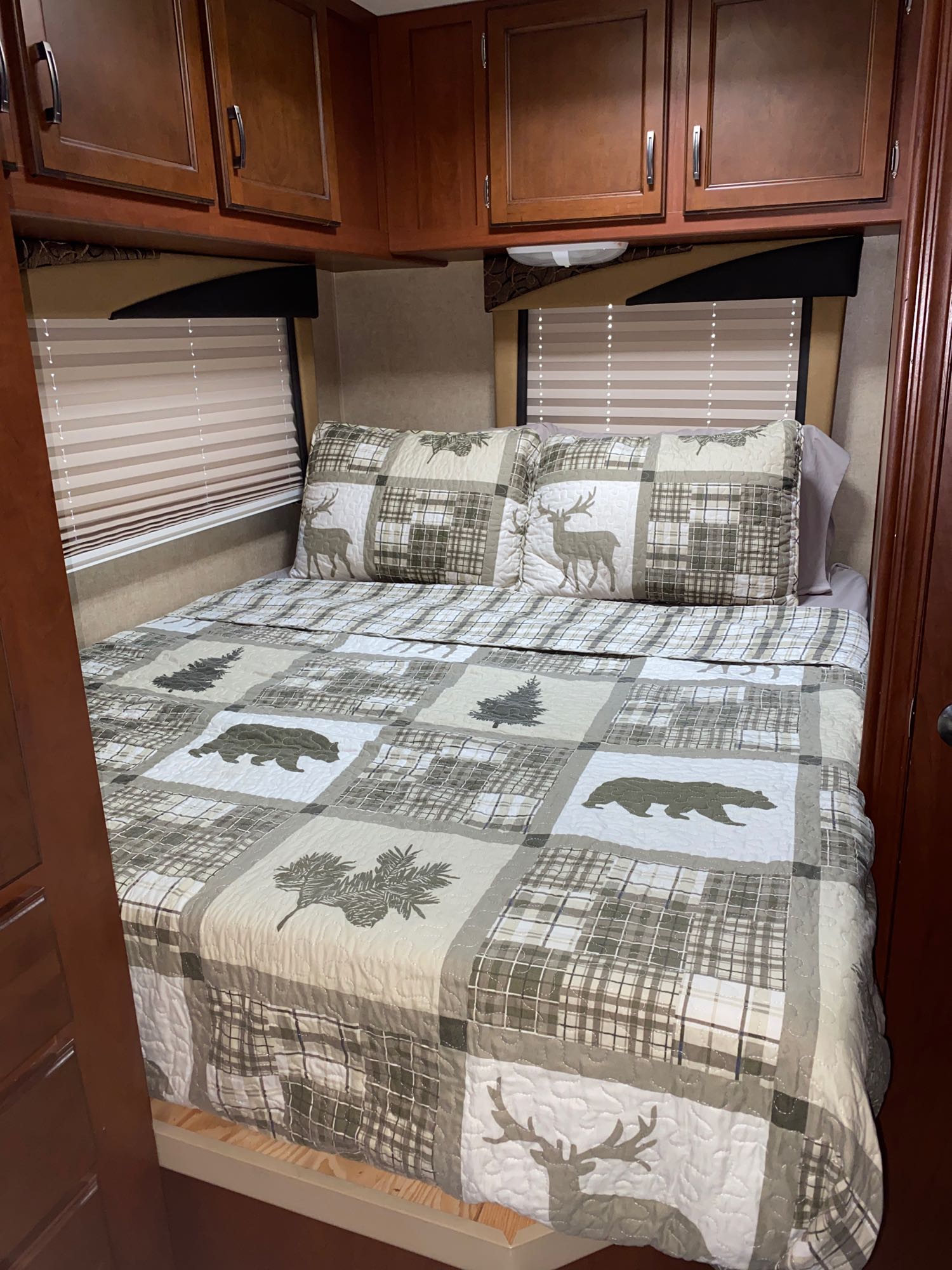 Cozy RV rental bedroom featuring a nature-themed quilt with bears and deer, overhead cabinets, and window blinds.. Jayco Redhawk 2014