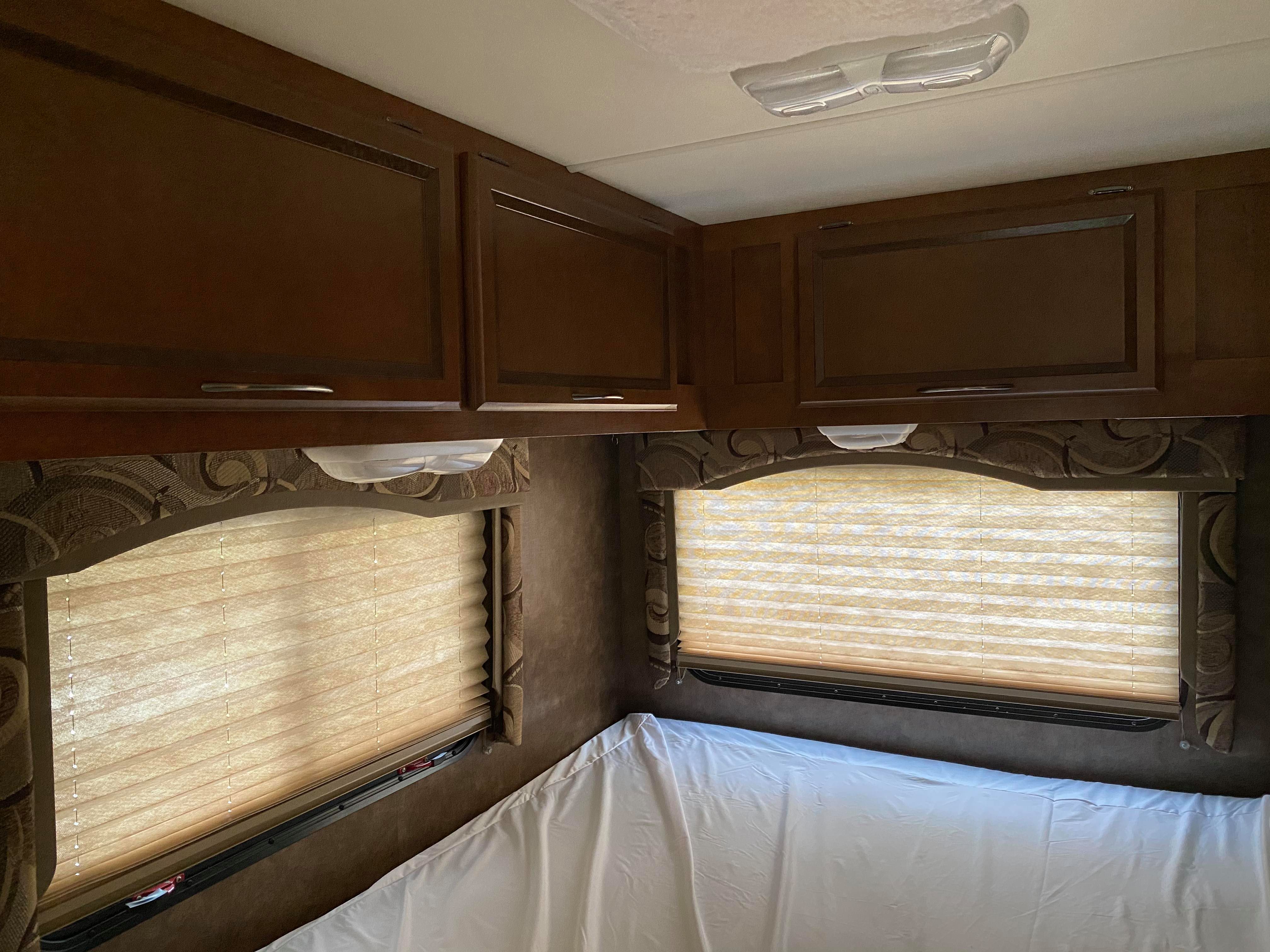 RV rental interior: bedroom with dark wood cabinets, pleated window blinds, and a white-covered bed.. Thor Motor Coach Four Winds 2013