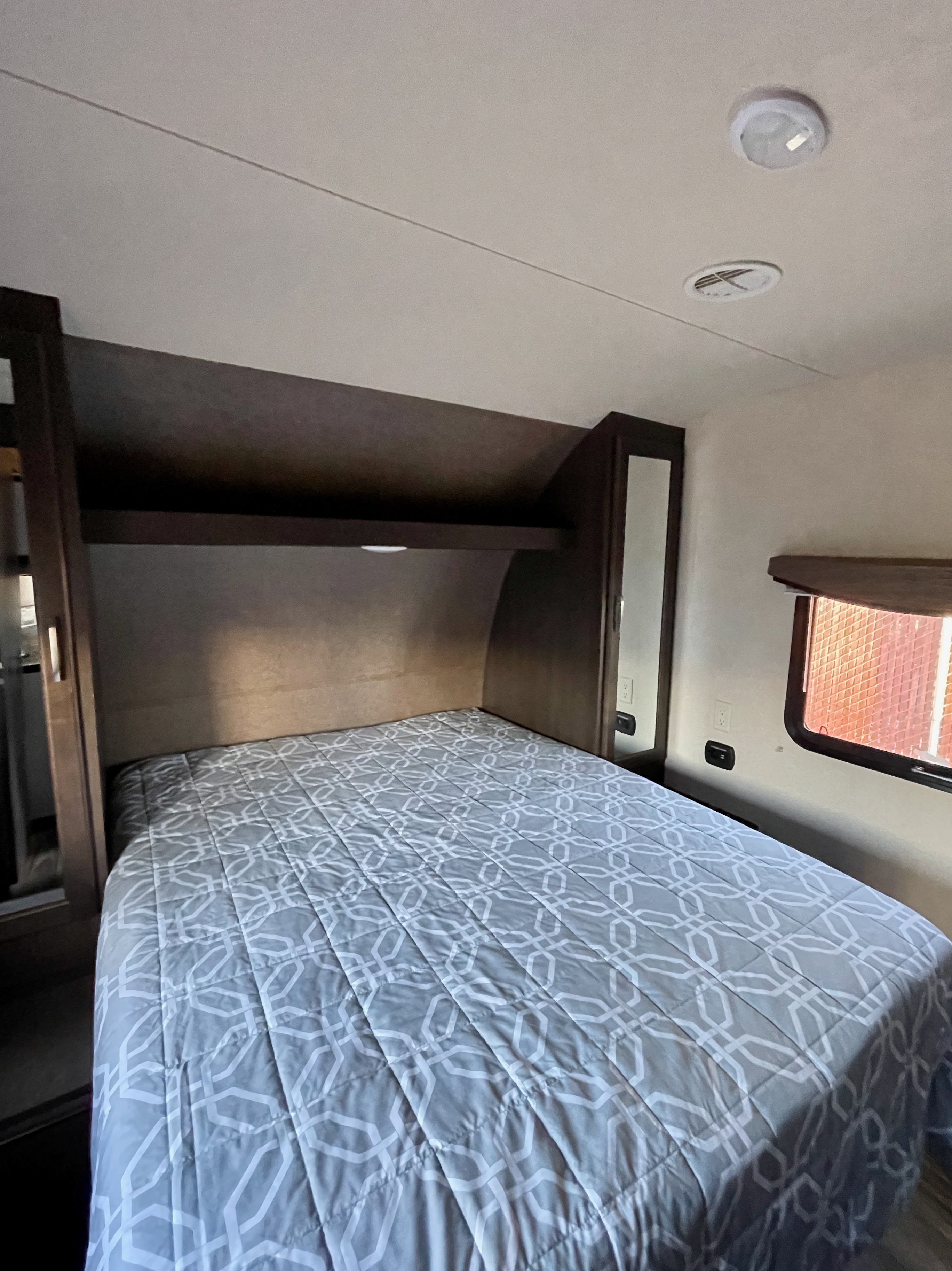 Comfortable RV rental bedroom with a grey patterned bed, built-in storage, and ceiling vents.. Forest River Evo T2550 2019